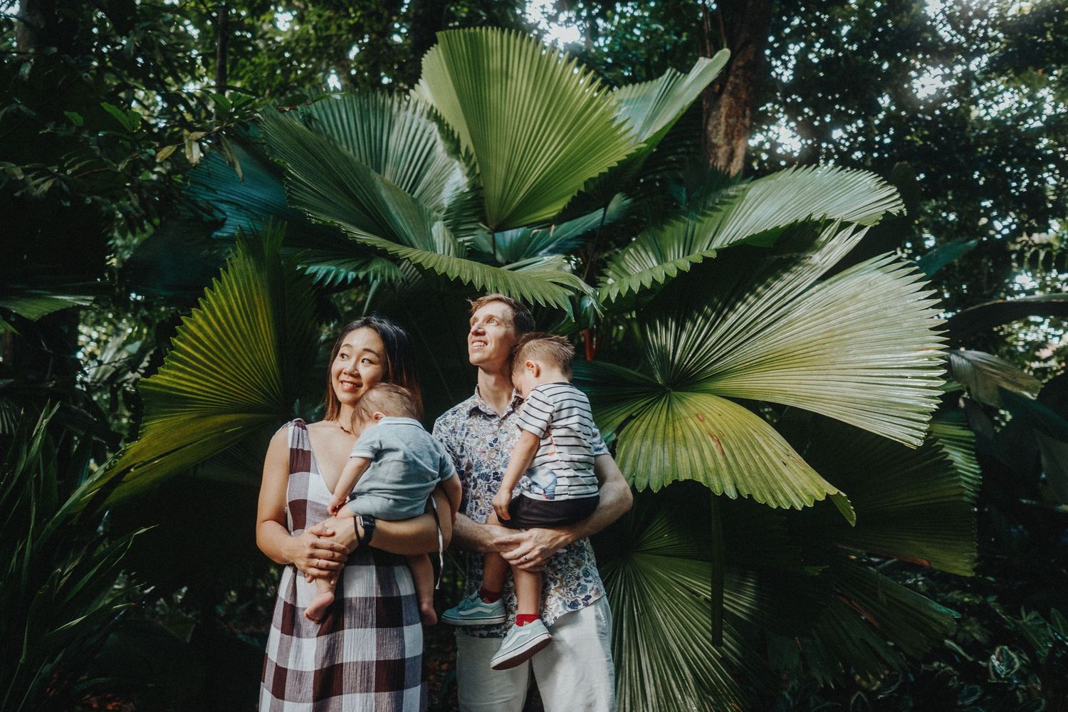 A family stands in front of large tropical palm fronds in an outdoor garden setting.