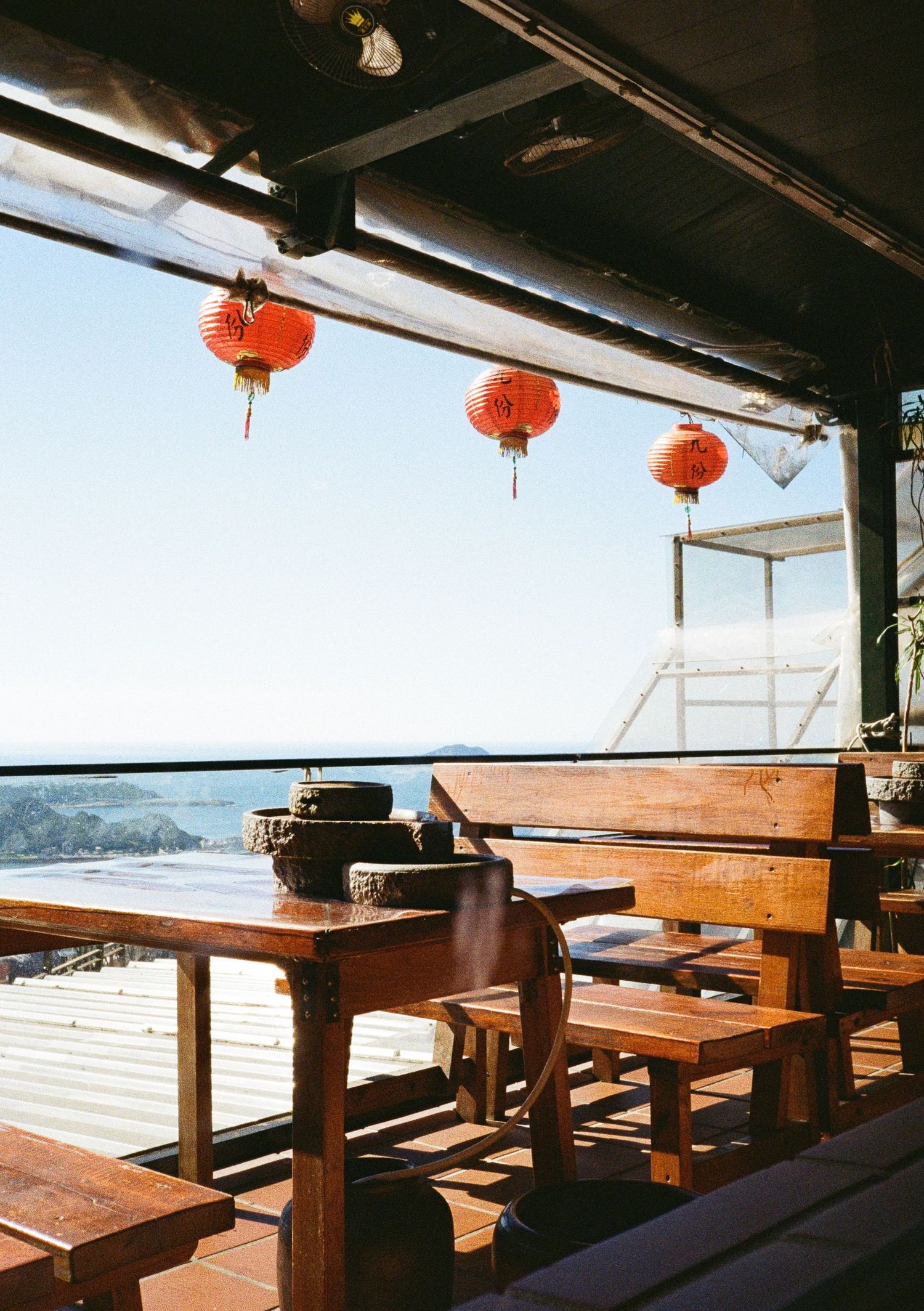 Outdoor wooden restaurant deck with benches and red lantern decorations overlooking a scenic view.