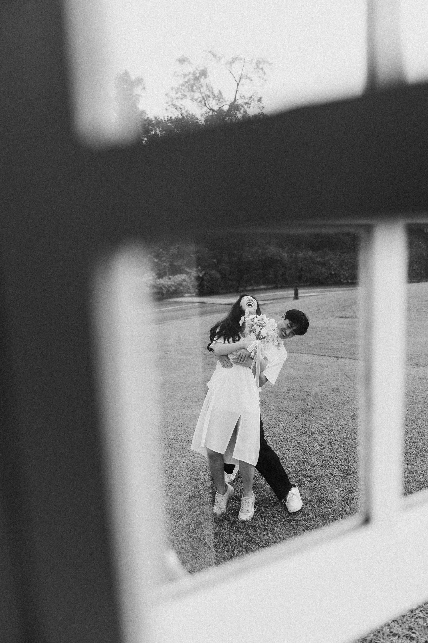 A playful couple captured through a window frame dancing on grass.