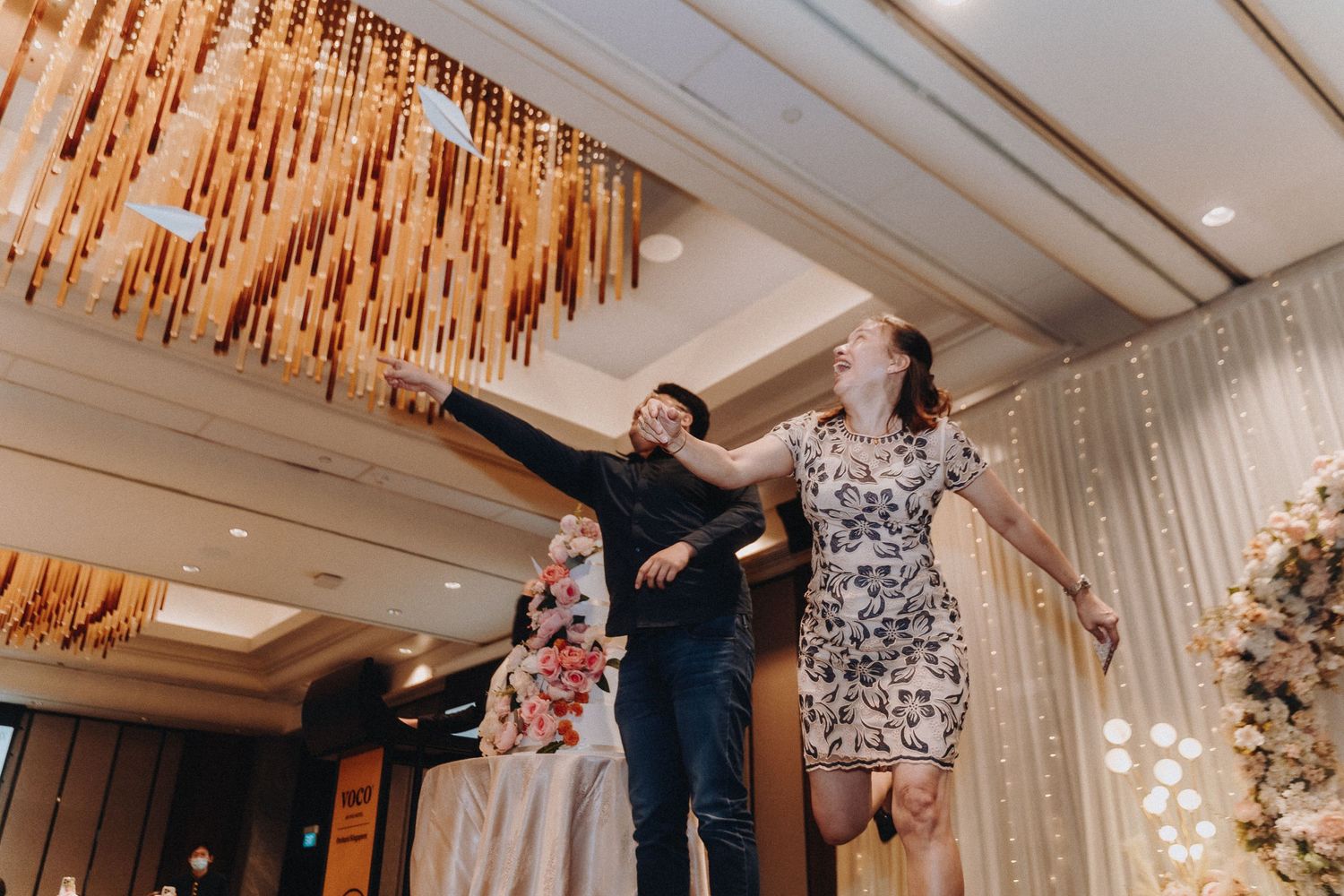 Wedding guests dancing energetically beneath a modern chandelier at an indoor reception venue.