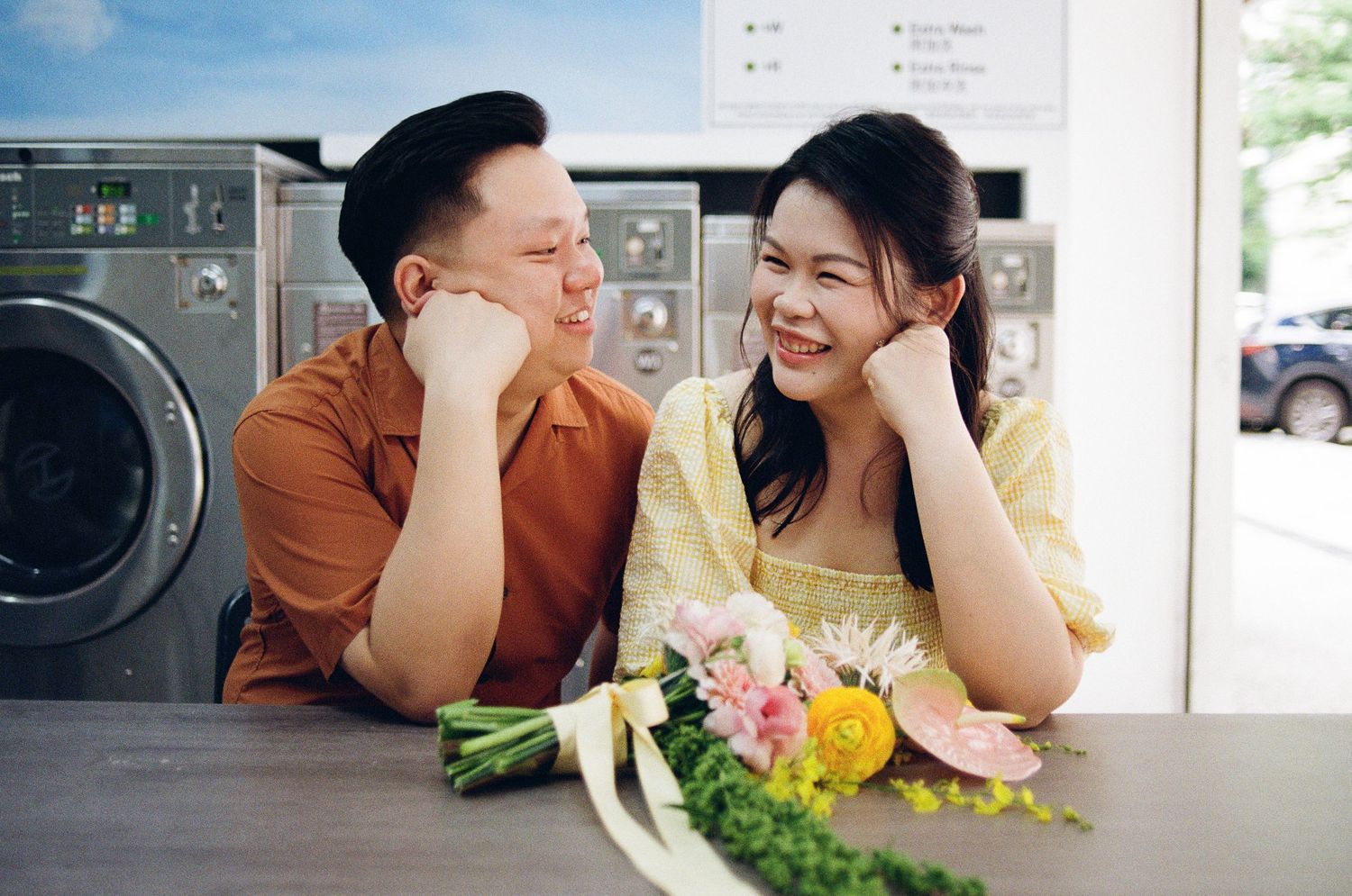 A romantic couple at a laundromat sharing a sweet moment with fresh flowers on the counter.