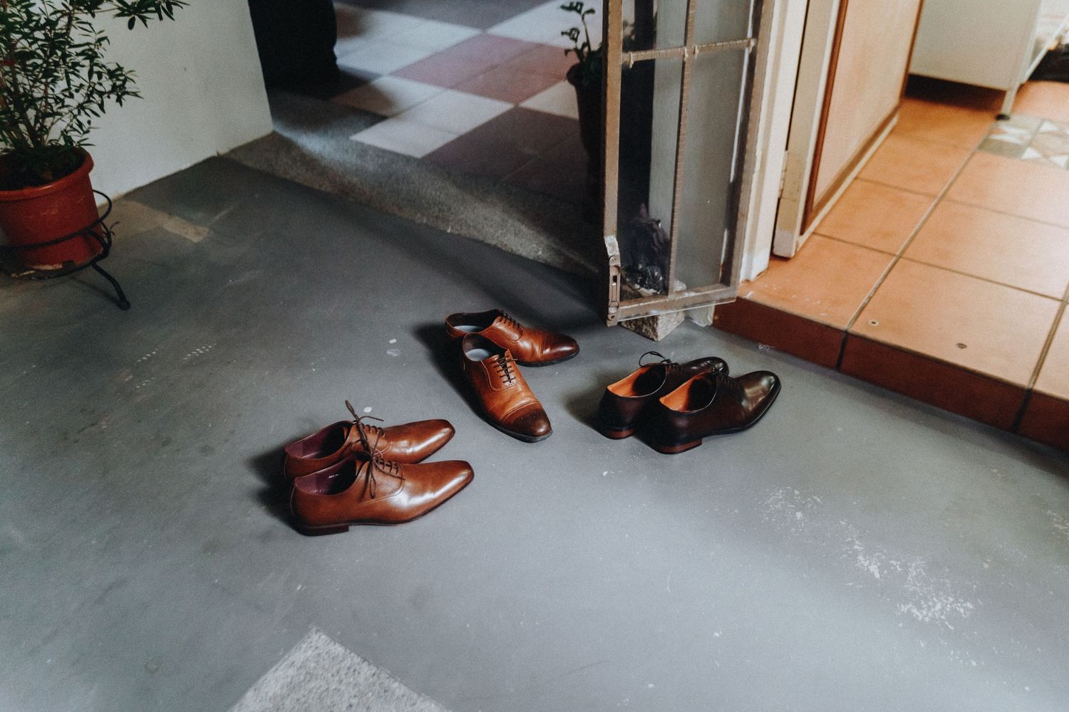 Several pairs of leather dress shoes arranged neatly at an entrance doorway on a concrete floor.