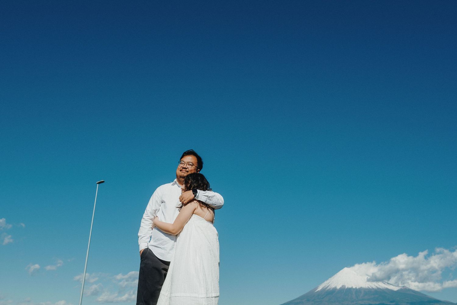 A romantic embrace against a backdrop of Mount Fuji and clear blue skies.