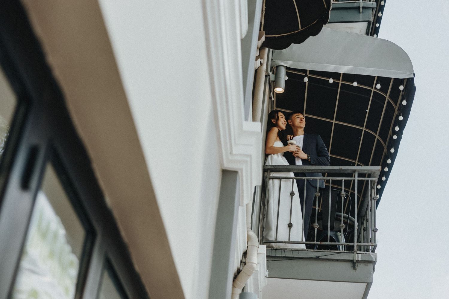 Romantic couple embraces on white ornate staircase under natural window lighting.