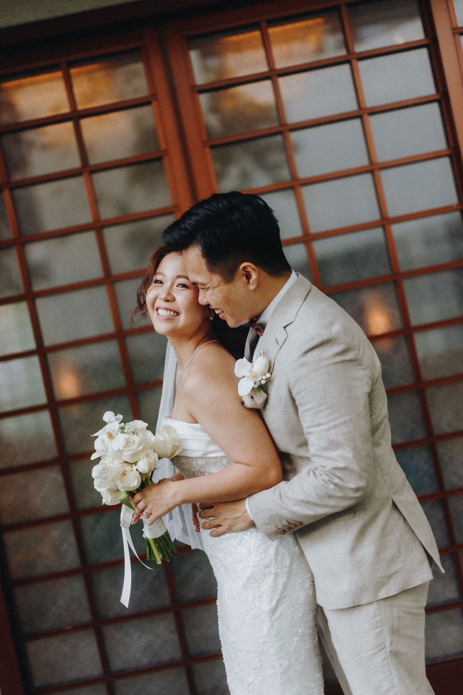 A couple embraces and laughs while posing for wedding photos in front of wooden panels.
