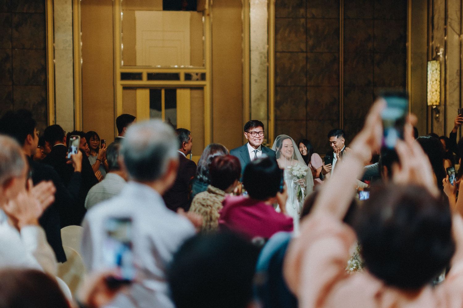 Wedding reception guests celebrate with raised hands in an elegant ballroom setting.