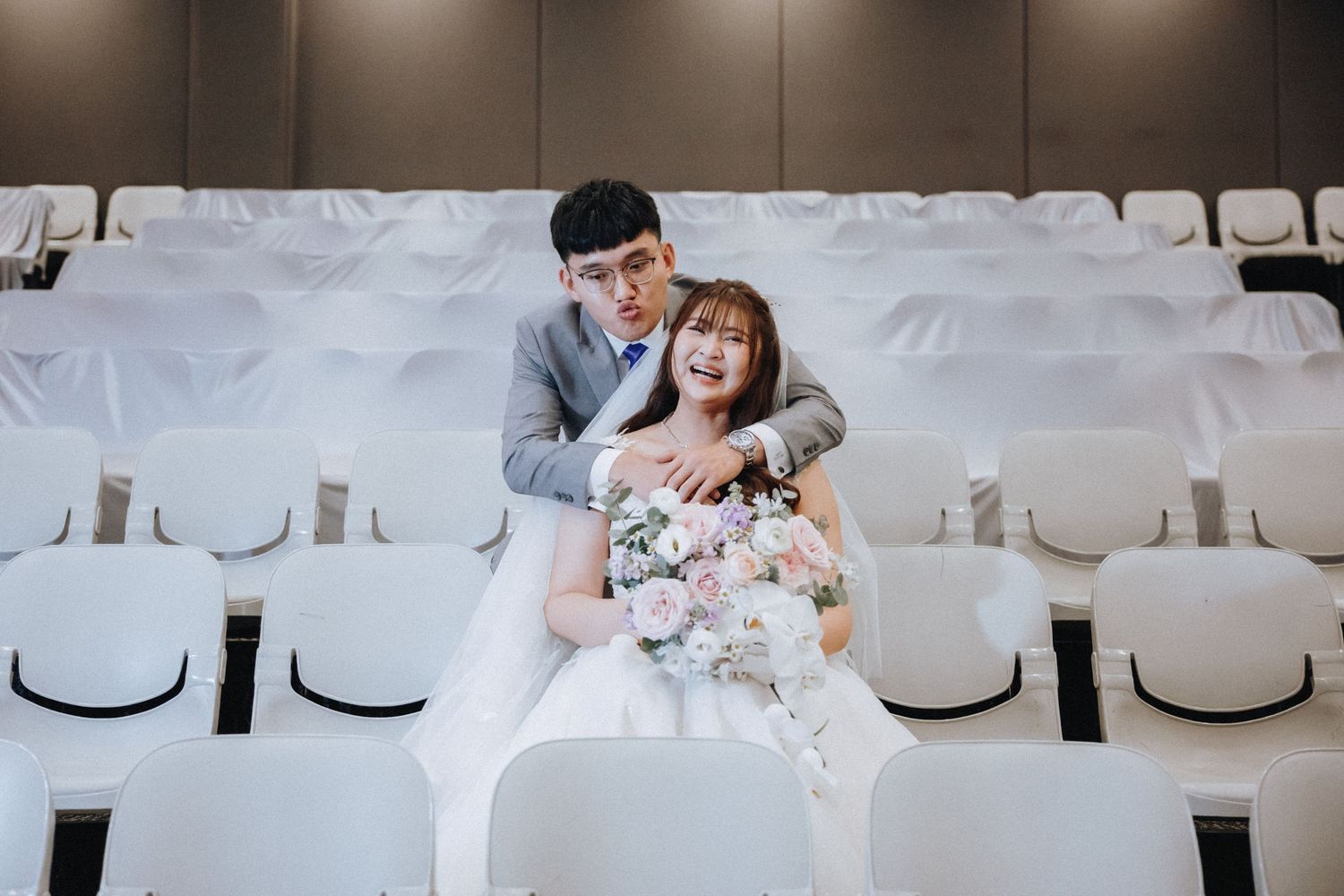 A couple shares an intimate moment while seated in white chairs at their wedding venue.