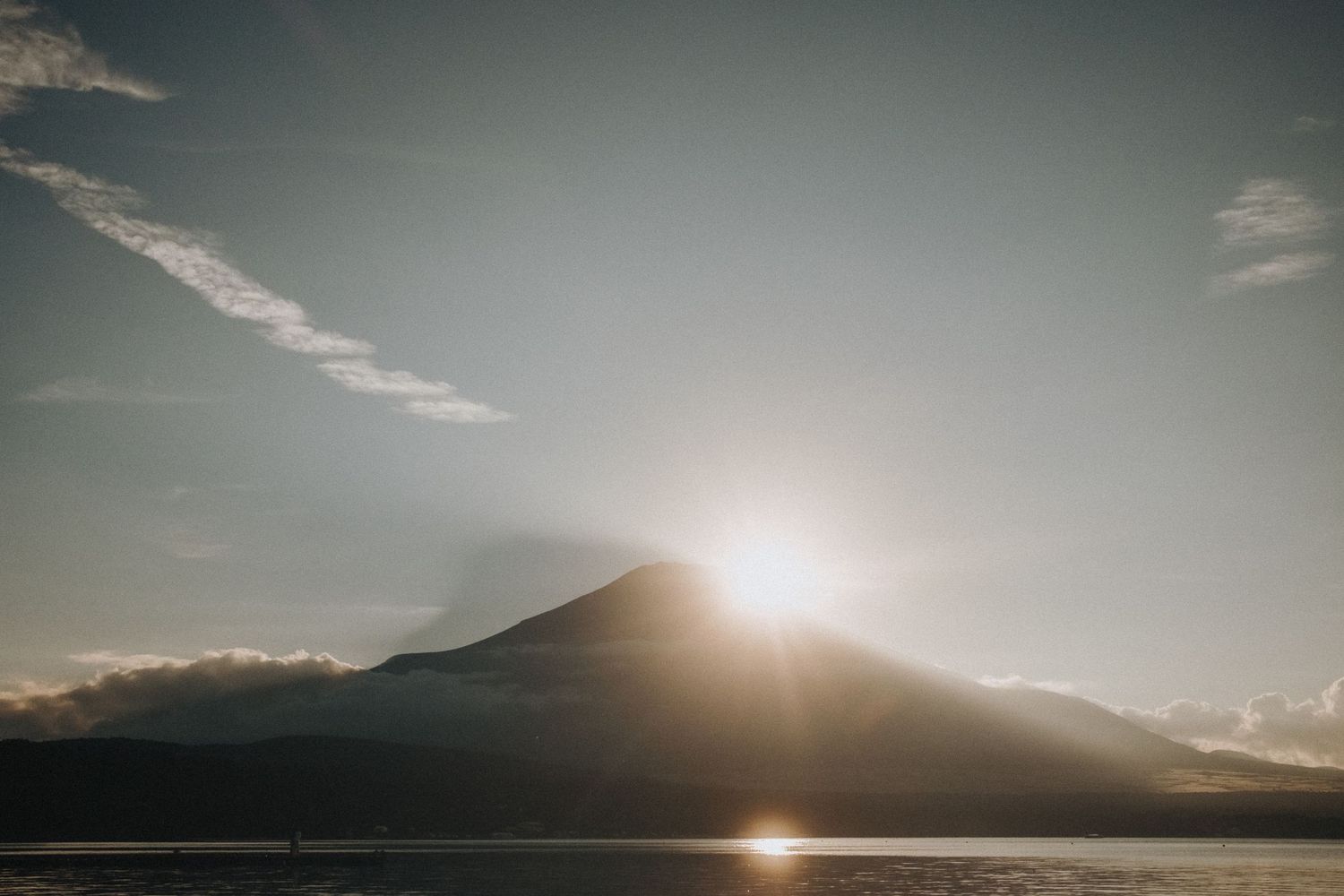 Dramatic sunset silhouette over mountain peaks with soft clouds.