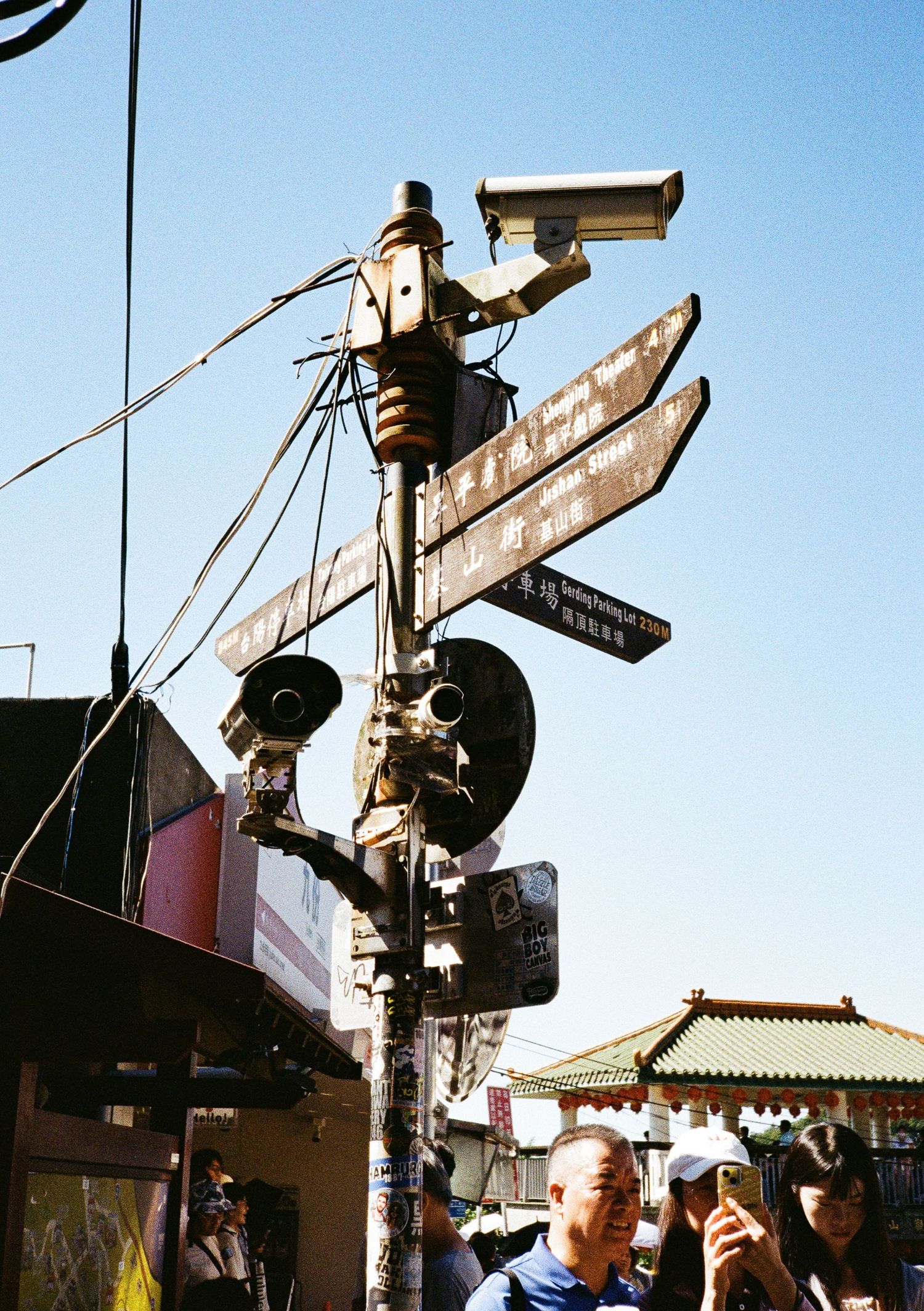Old street signs intersect at various angles against a bright sky in an urban setting.