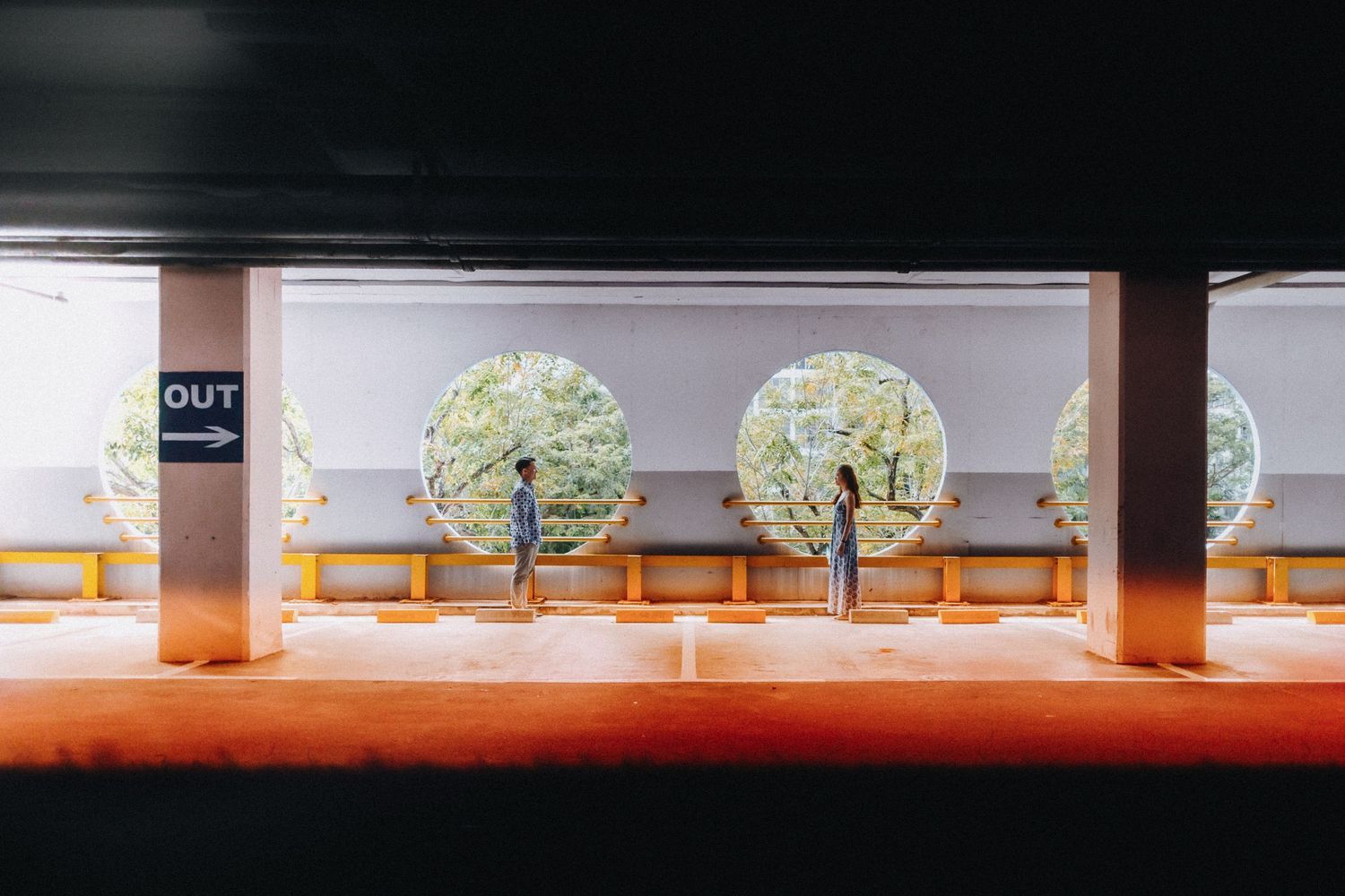 Illuminated decorative trees line a modern parking garage with orange floor and concrete pillars.