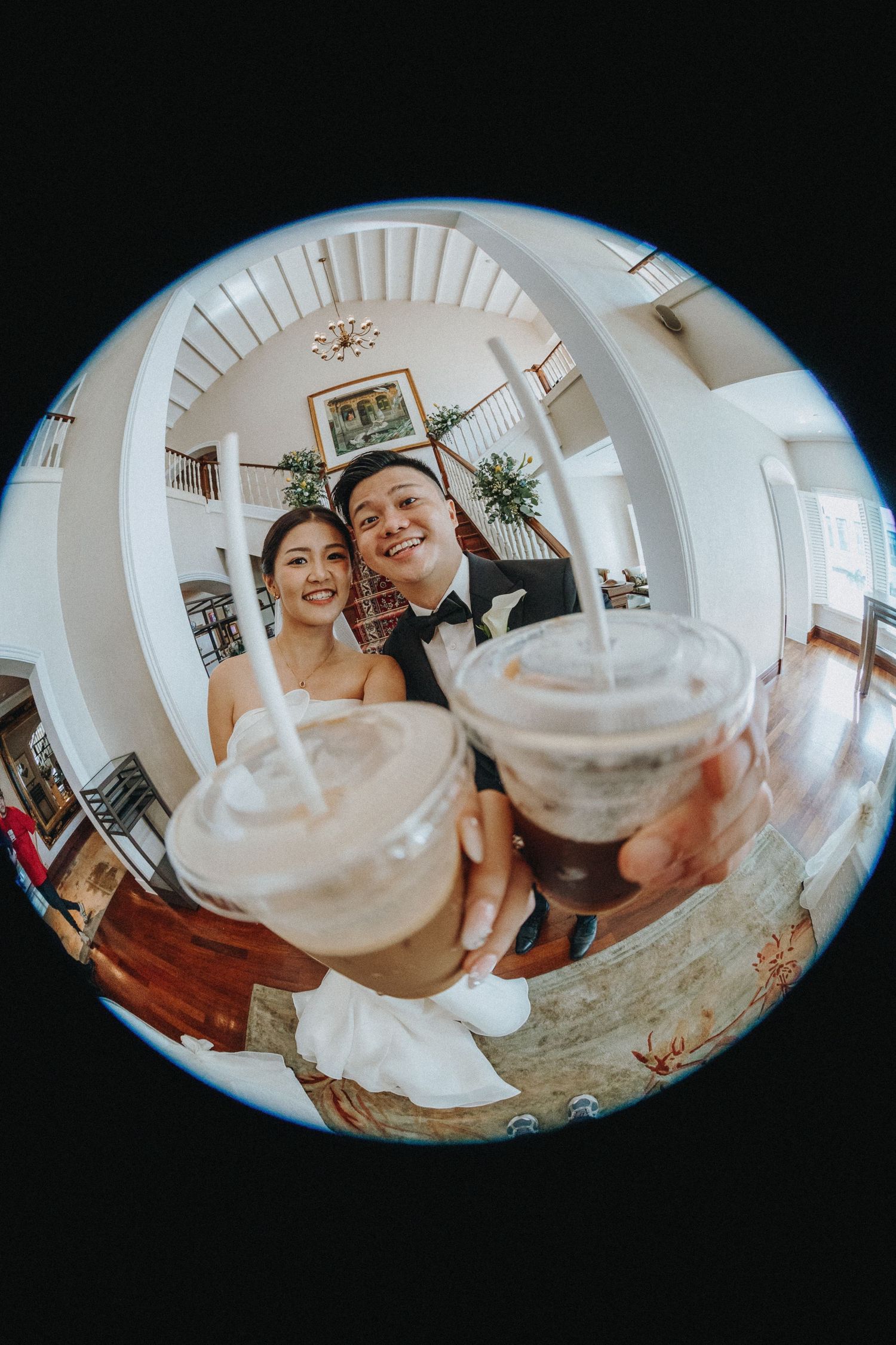 A fish-eye lens captures a couple toasting with iced drinks during their wedding celebration.