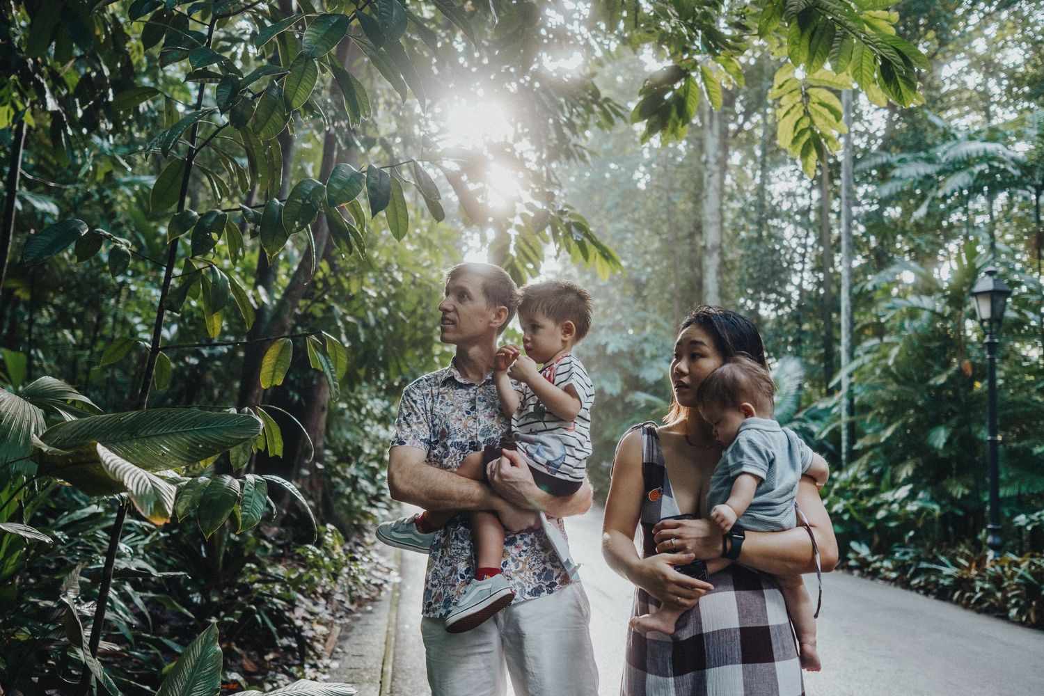 A family walks together along a lush tropical garden path on a sunny day.