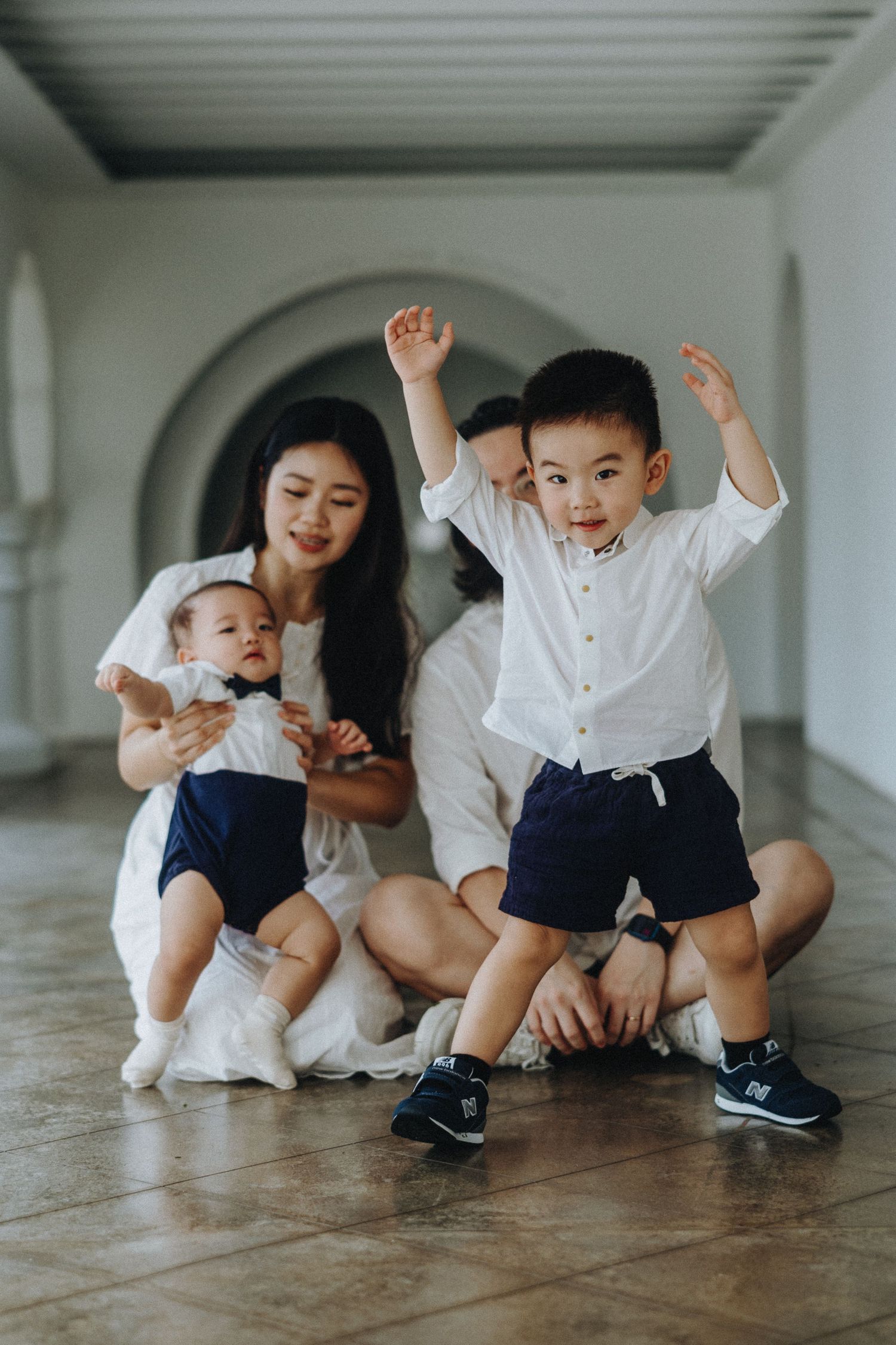 Children in coordinated white and navy outfits play energetically while being photographed in an elegant hallway.
