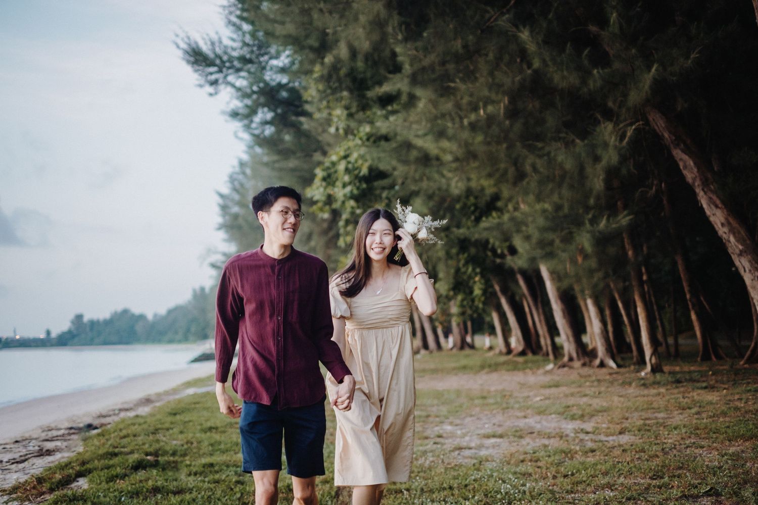 Romantic couple walking along a scenic beach path with swaying palm trees and ocean views at sunset.