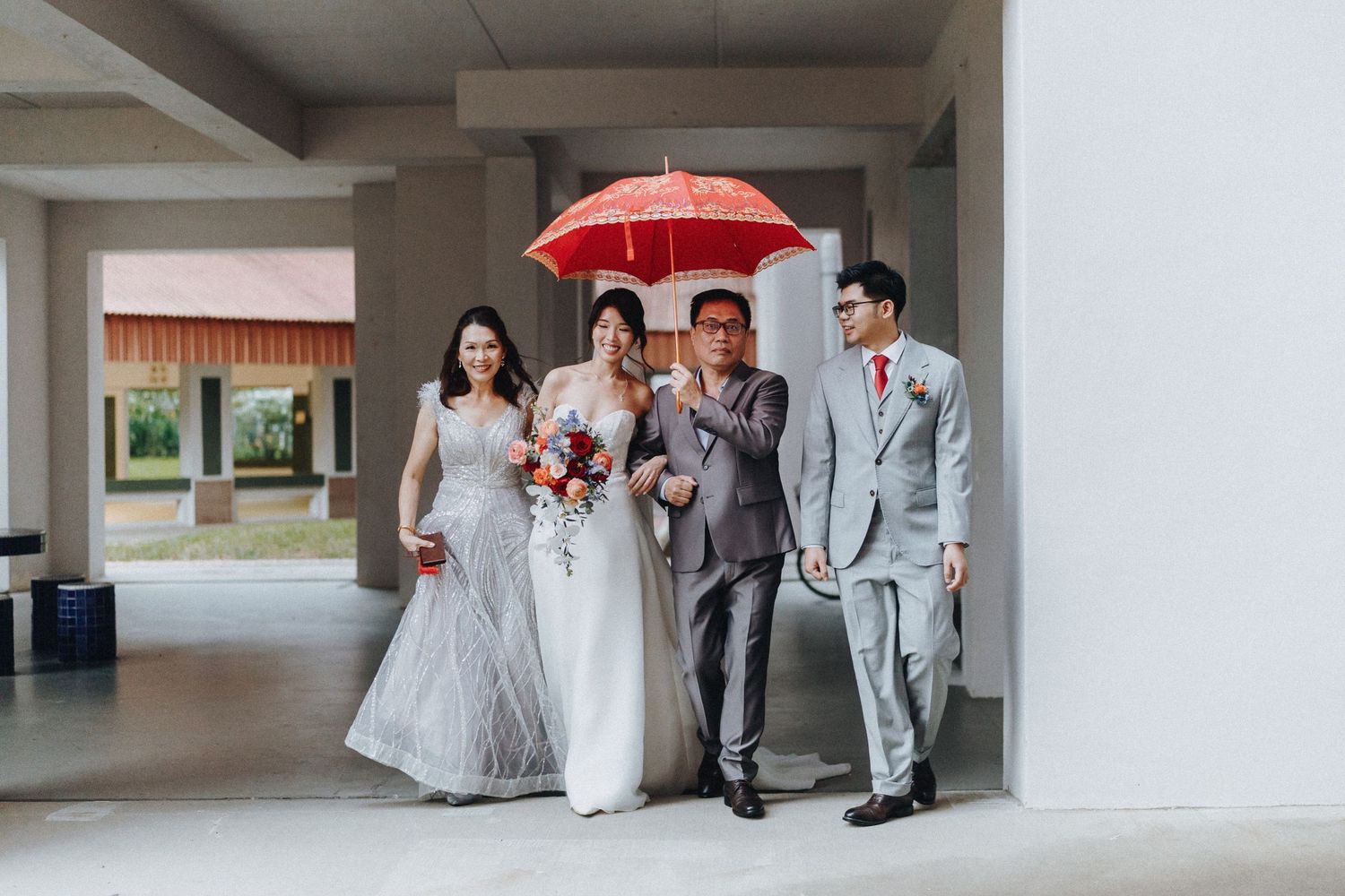Wedding party walking together under a red umbrella in a covered walkway.