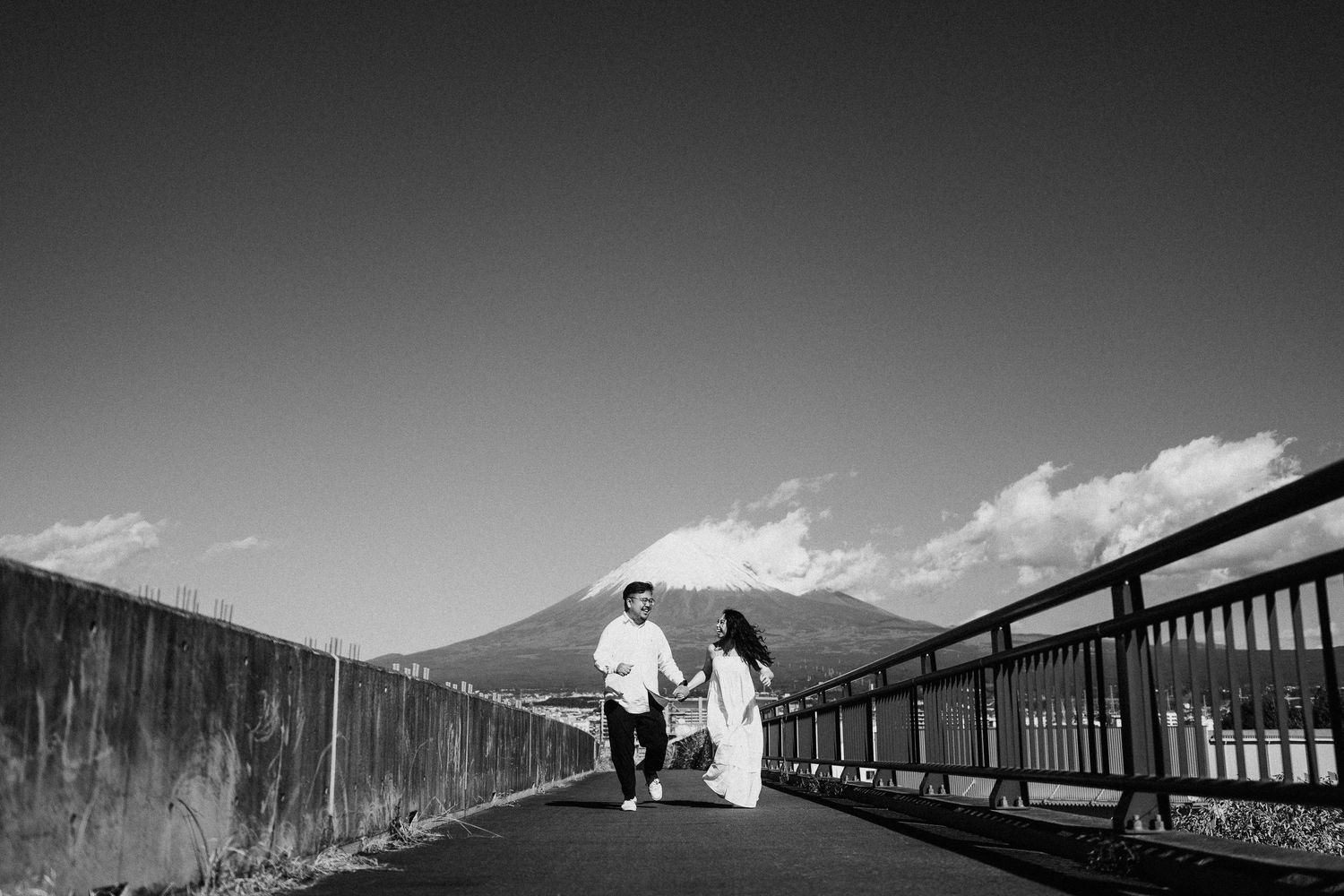 Black and white silhouette of people walking across an elevated bridge or walkway.
