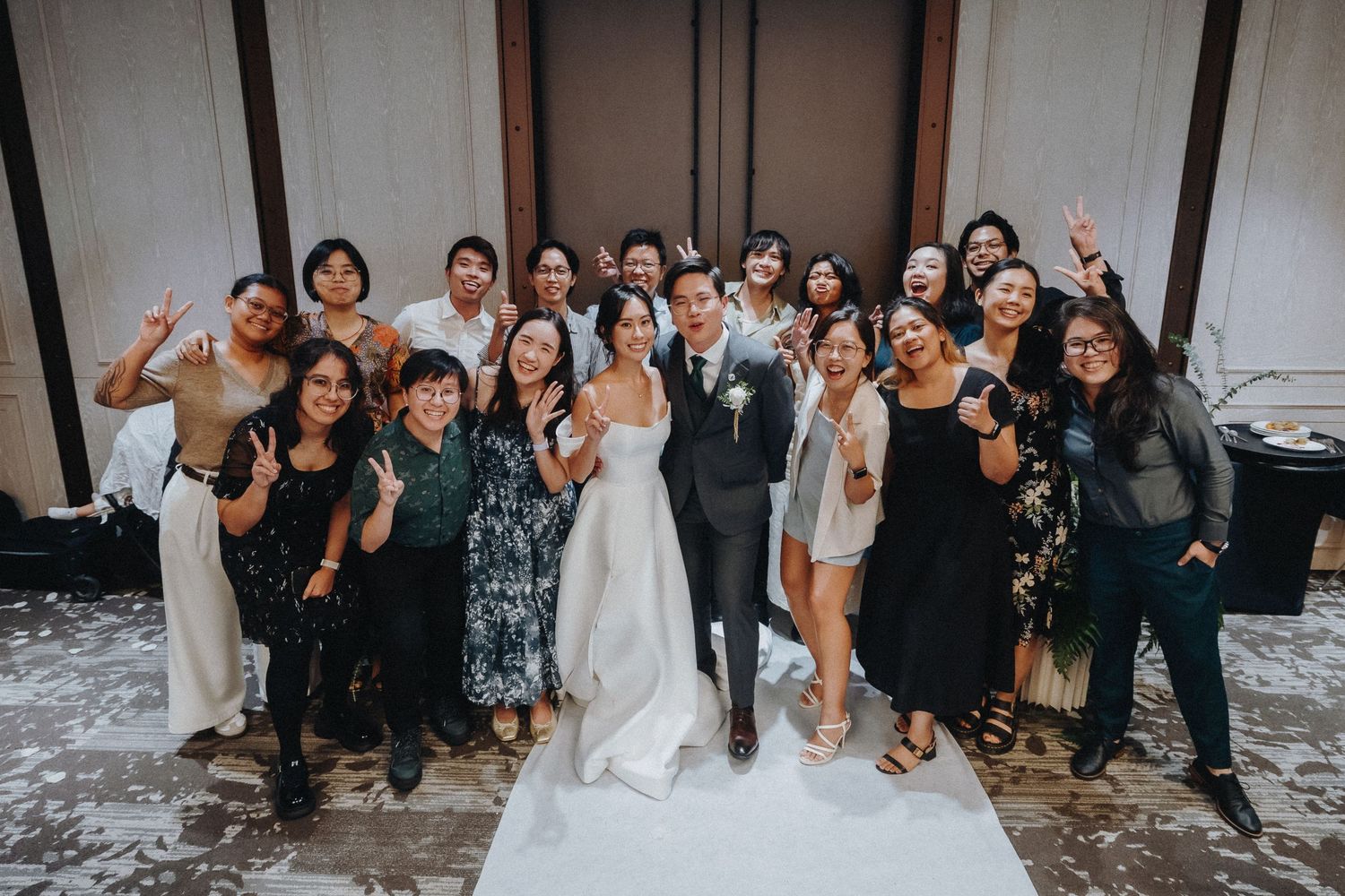 A large wedding party poses together for a celebratory group photo in formal attire.