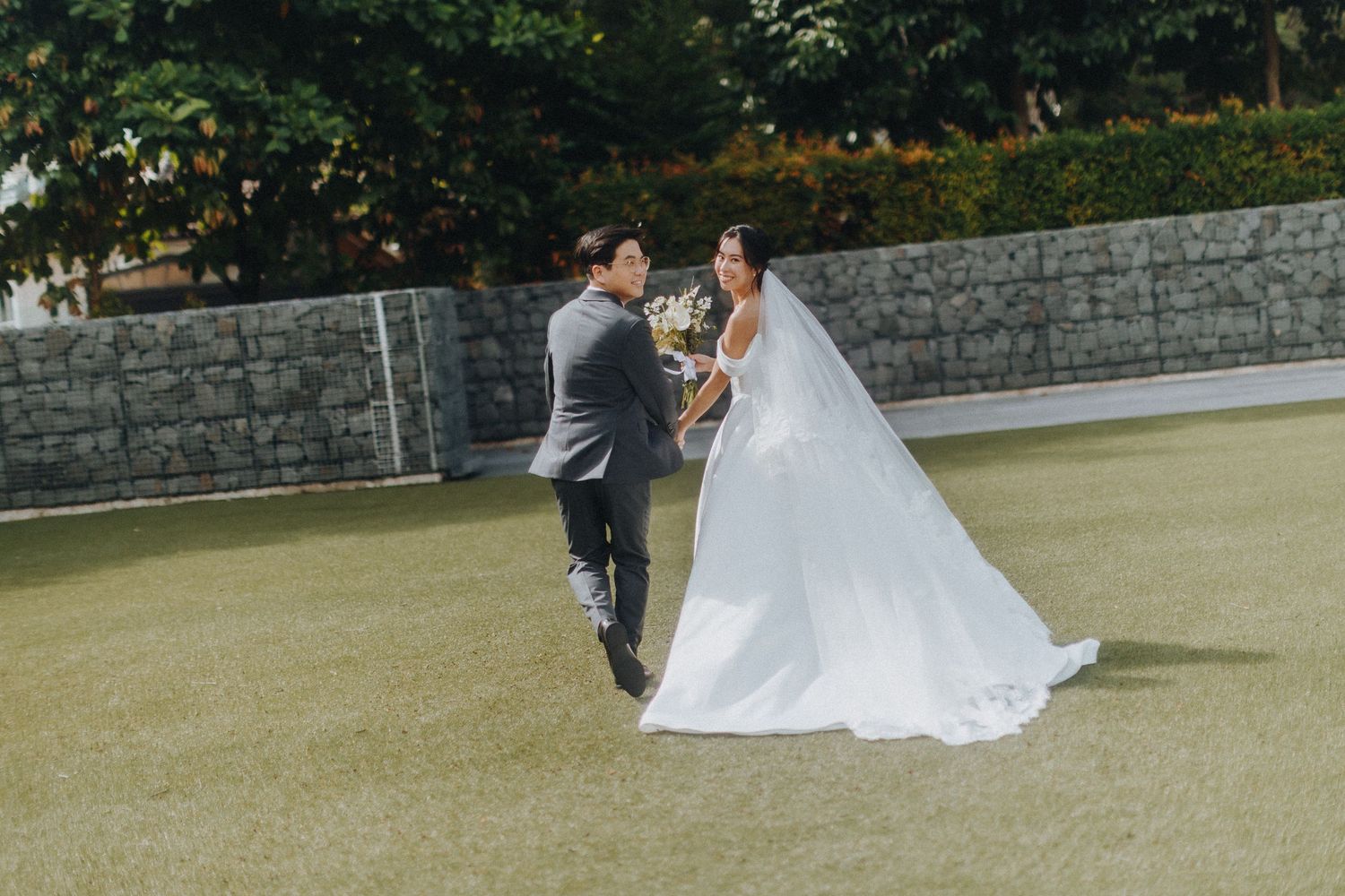 A wedding couple spins gracefully on an outdoor lawn surrounded by stone walls on a sunny afternoon.