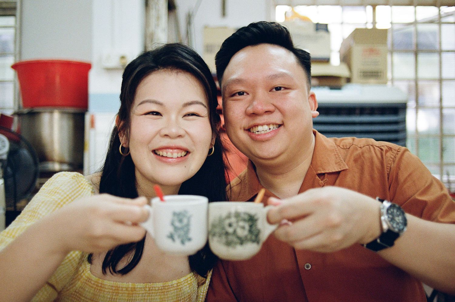 Two people smiling while toasting with Starbucks coffee cups in a casual indoor setting.