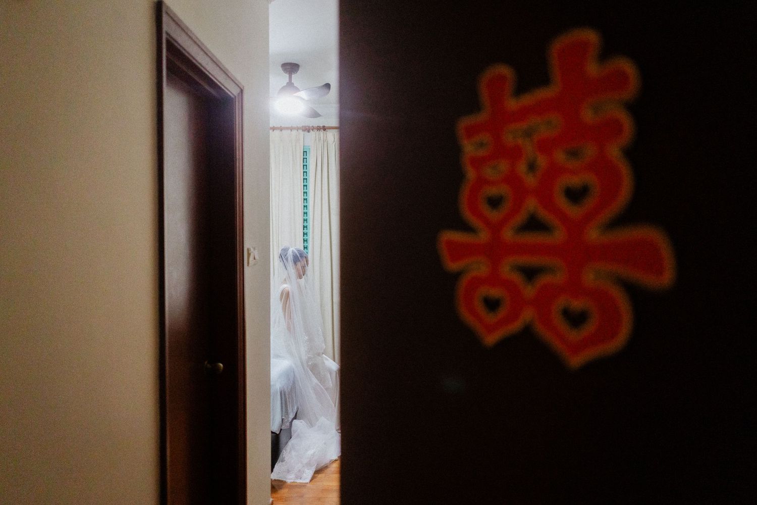 Chinese double happiness symbol on door with bride getting ready in background.