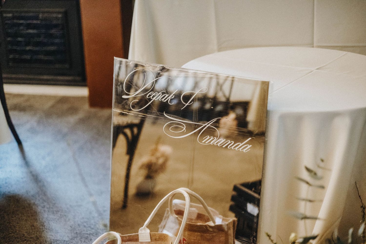 Elegant acrylic wedding sign with script names Deepak and Amanda displayed at a reception venue.