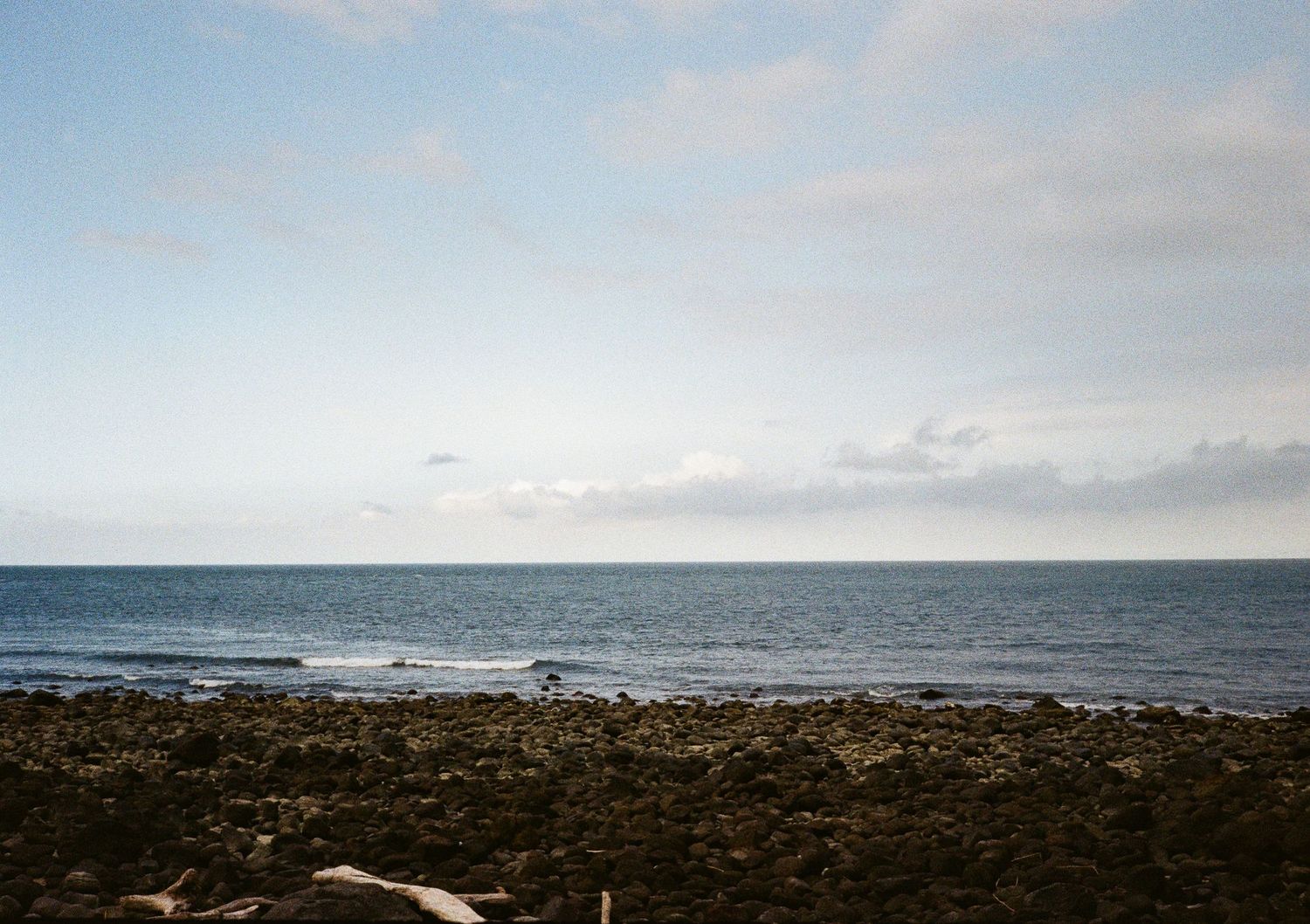 Rocky coastal shoreline meeting the ocean horizon under a pale blue sky.