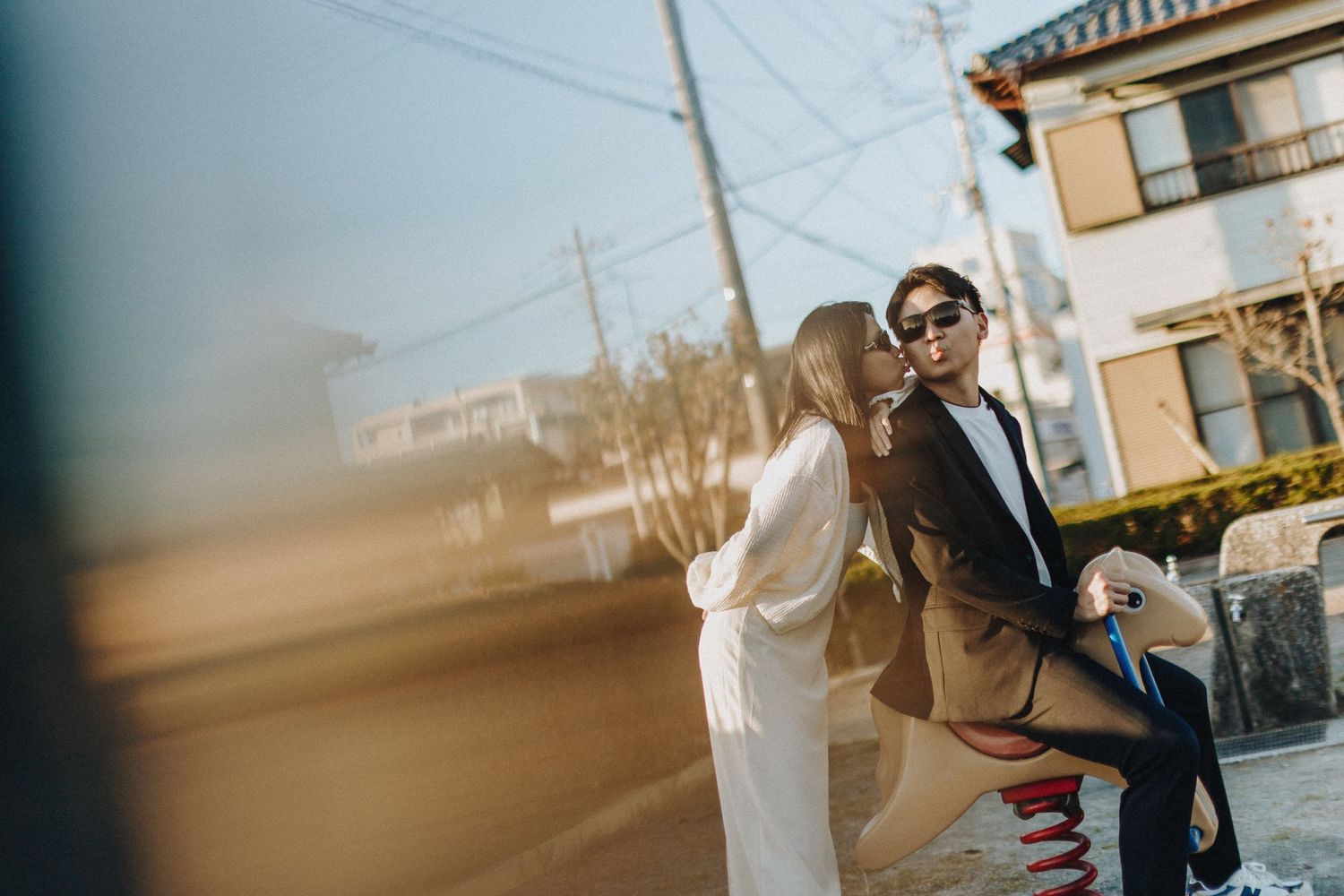 A couple in formal attire posing together on a sunny day in a residential neighborhood.