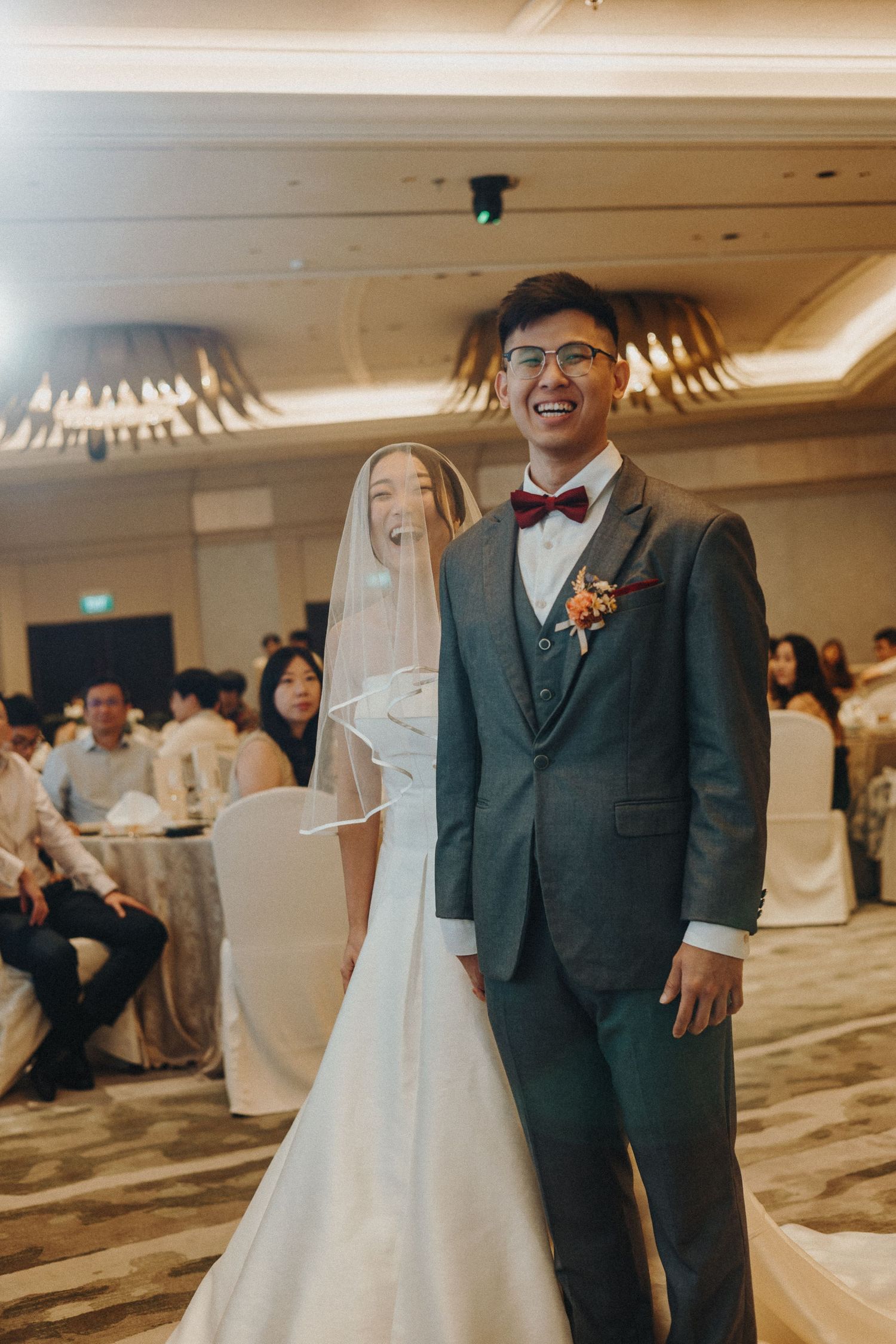 Bride and groom share joyful moments in a wedding reception hall with elegant lighting and decor.