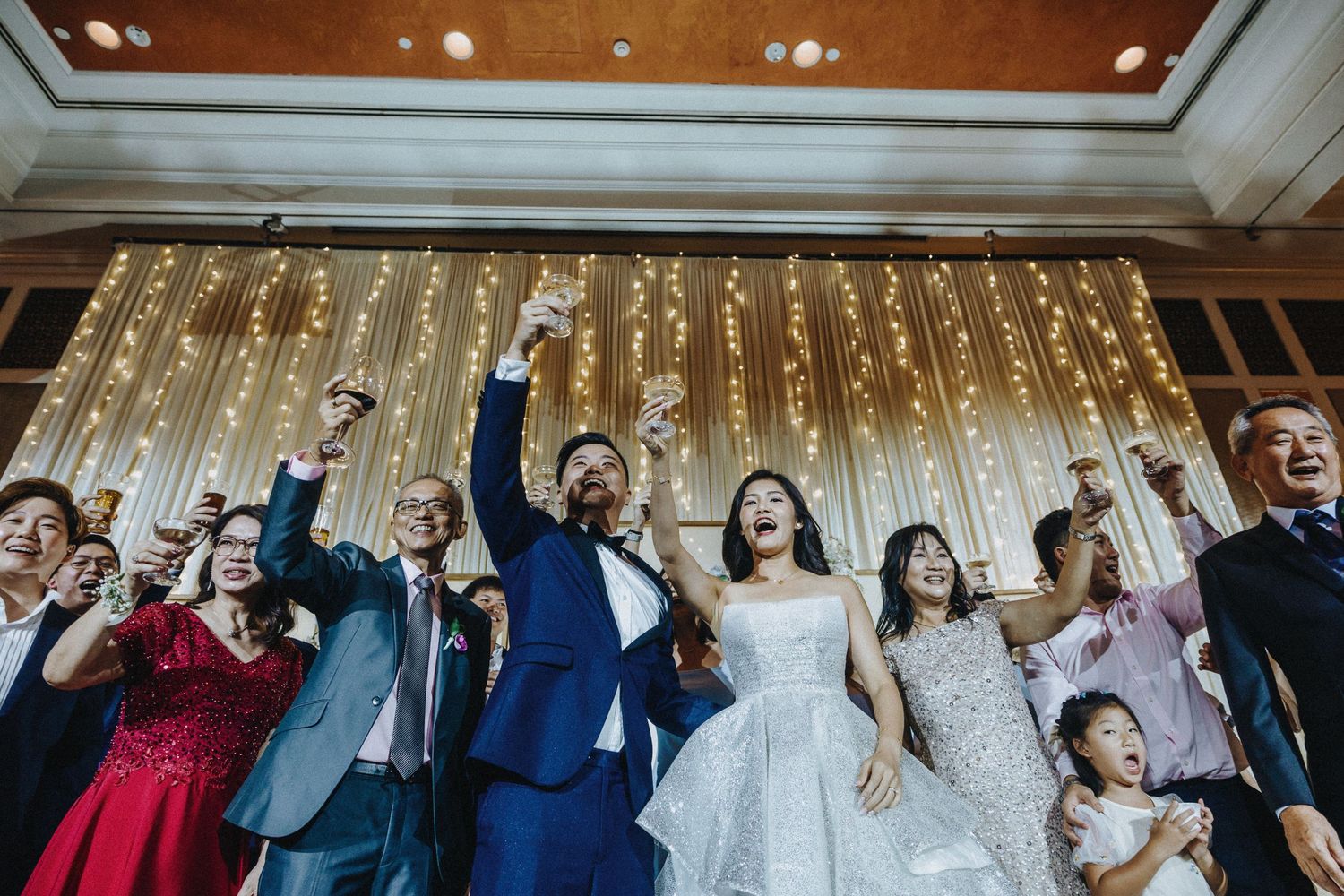 Wedding celebration with guests cheering in front of a sparkly golden light backdrop.