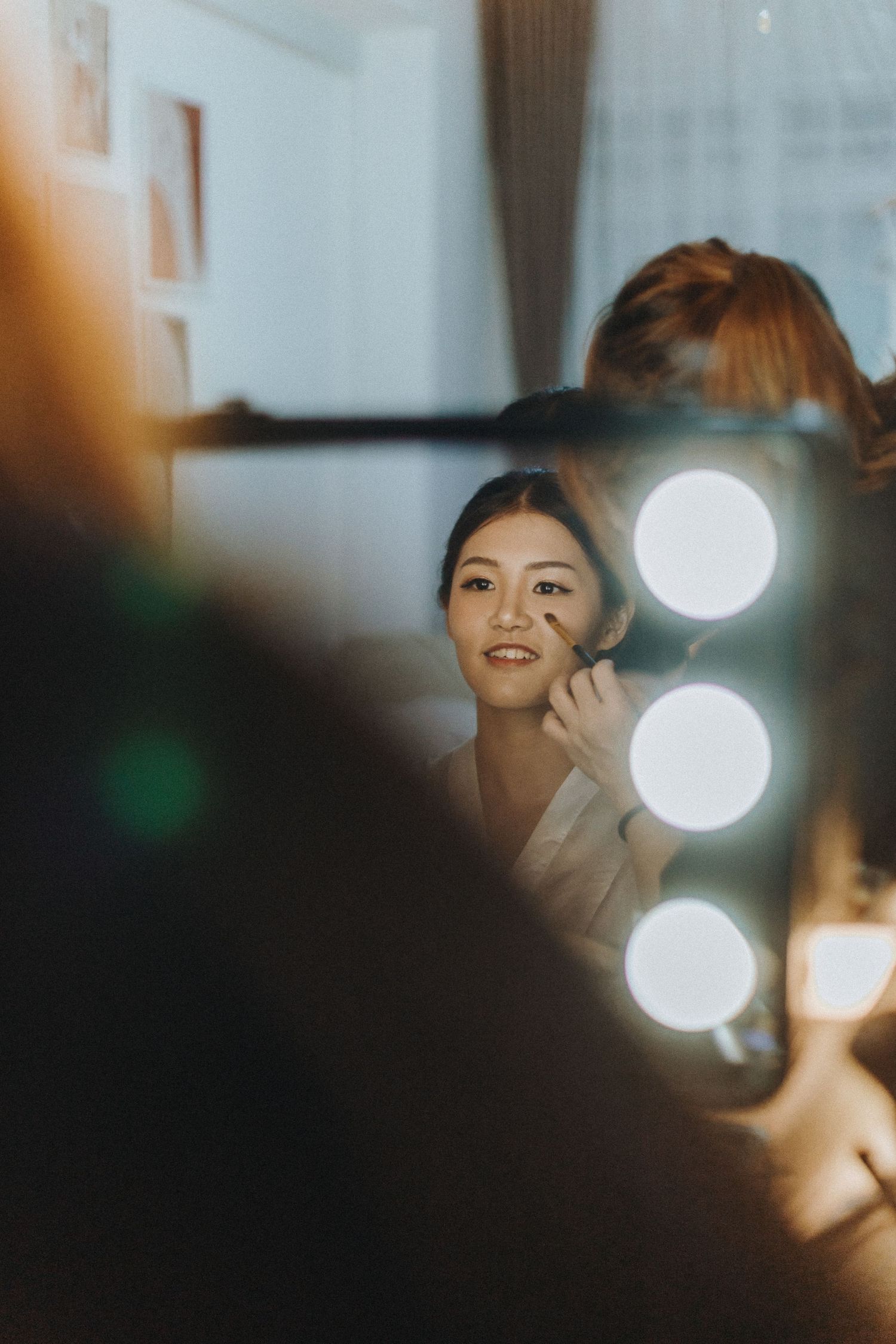 Makeup preparation scene with bright vanity mirror lights reflecting in a softly lit room.