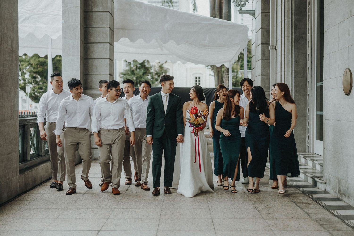 Wedding party and guests gathered in an elegant columned corridor with natural lighting.