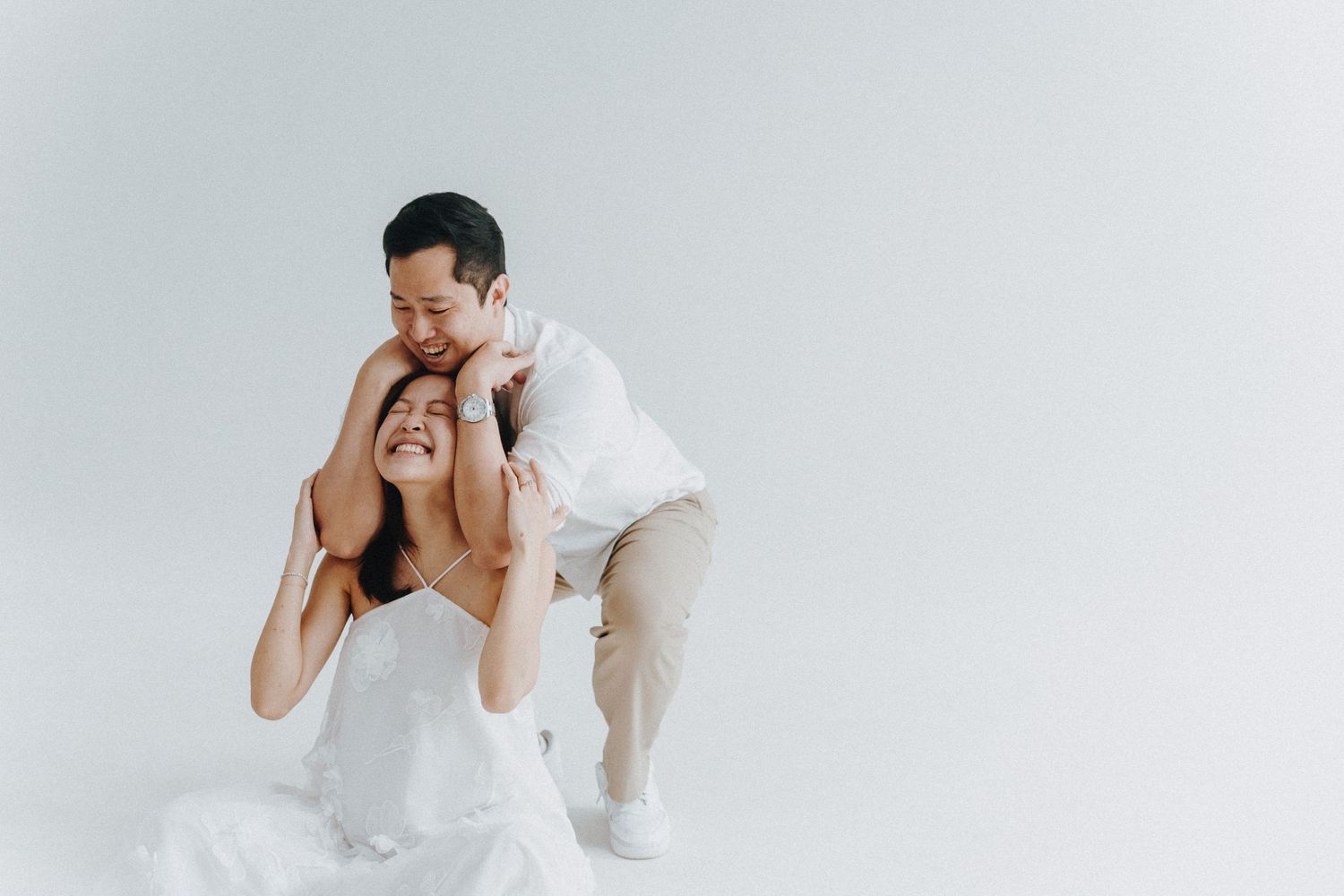 Two people in a playful pose against a white background wearing matching light-colored outfits.