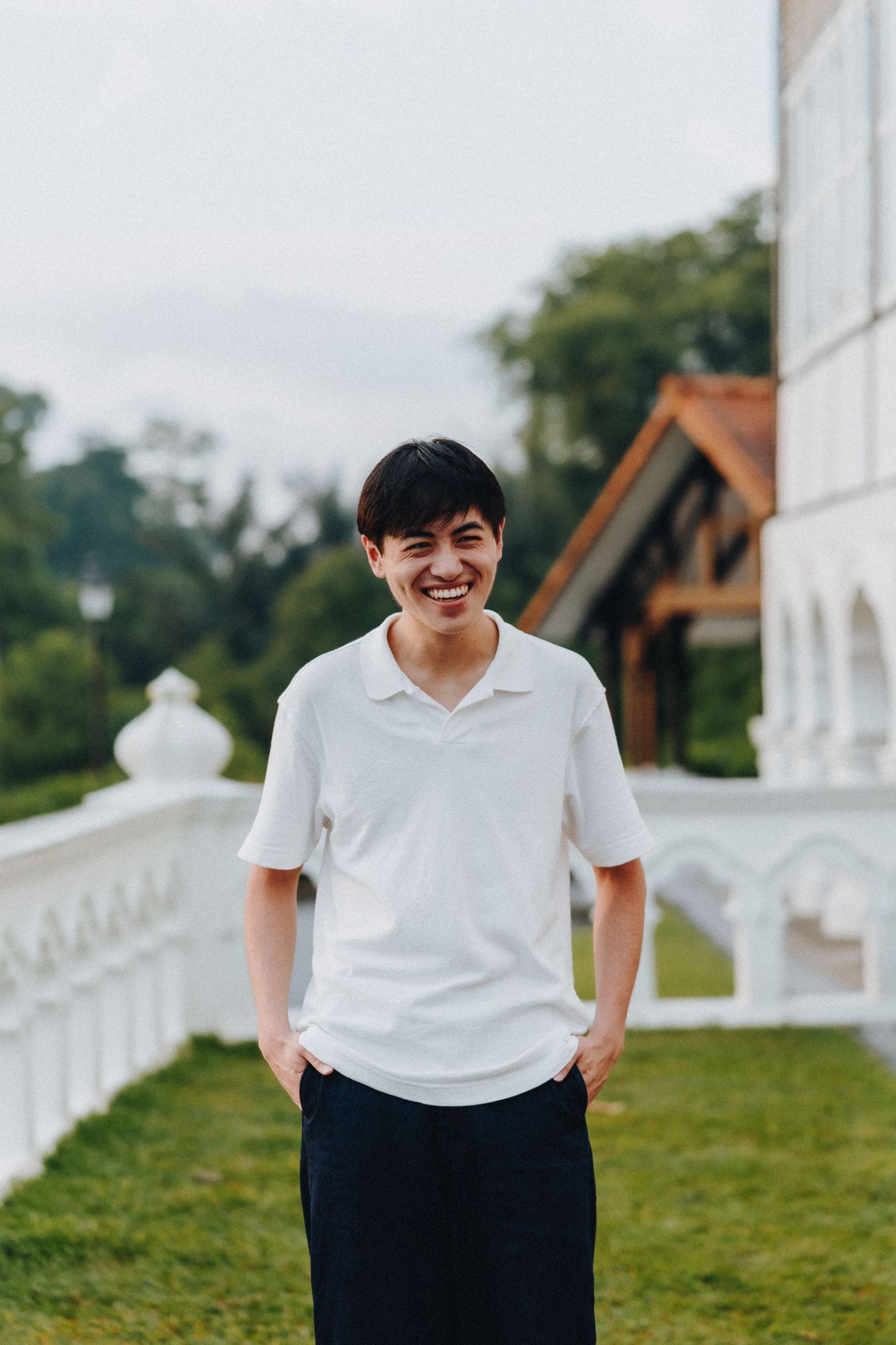A person in a white polo shirt and black pants smiles joyfully outdoors.