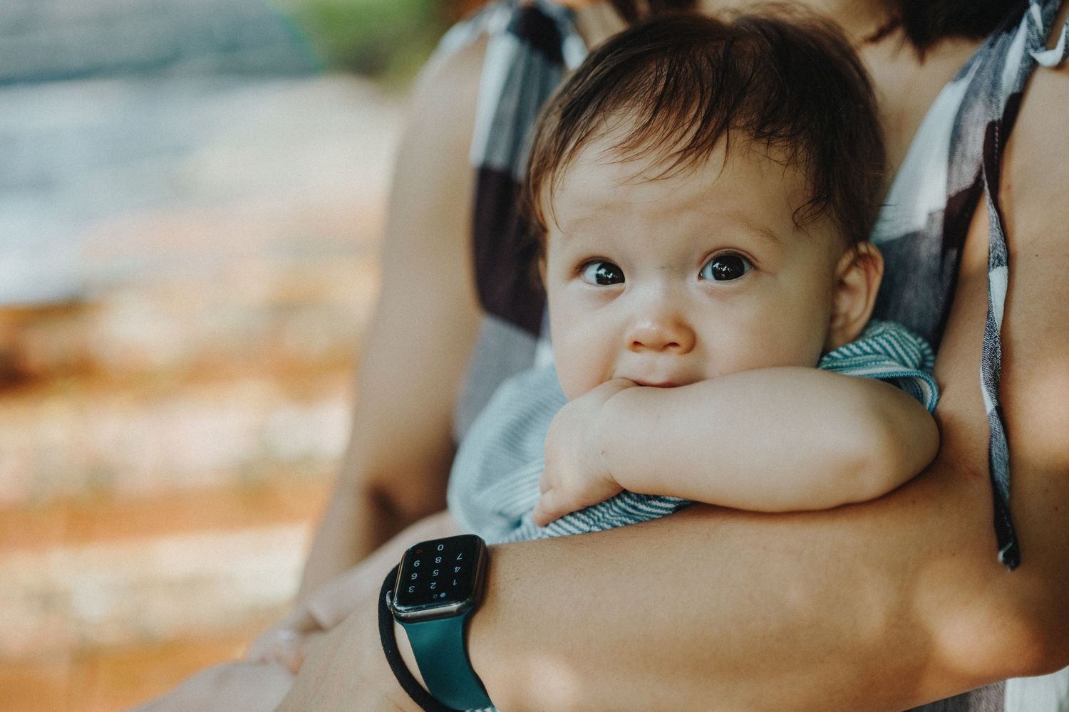 A baby in a teal outfit smiles and plays while being held against a light-colored background.