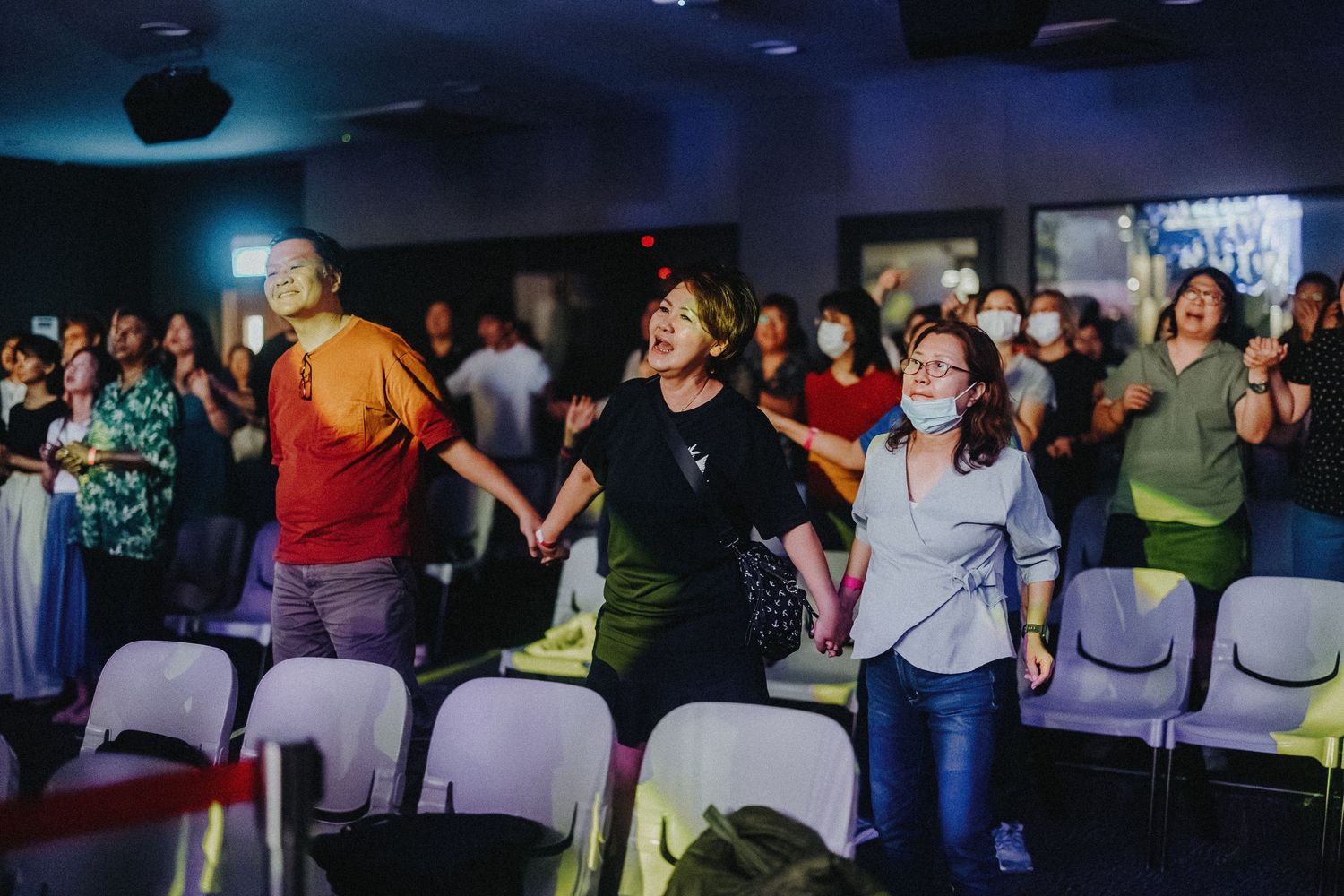 Concert attendees dance and worship together in a venue with rows of chairs.