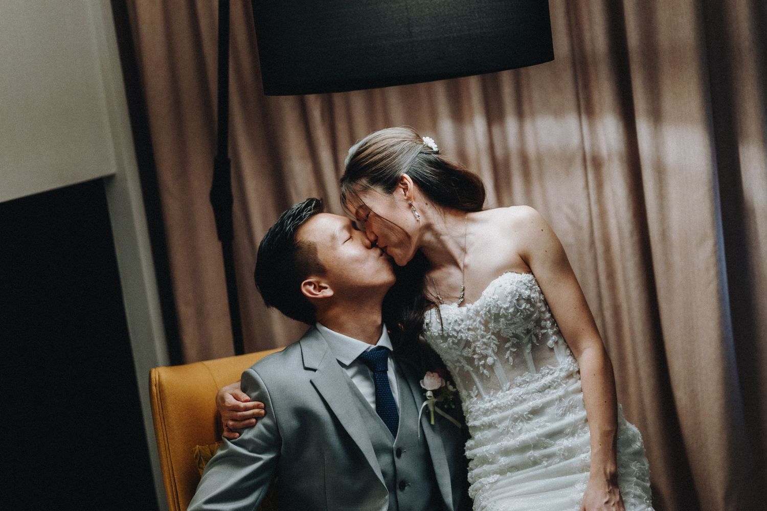 Romantic wedding moment captured in indoor setting with warm lighting and neutral backdrop.