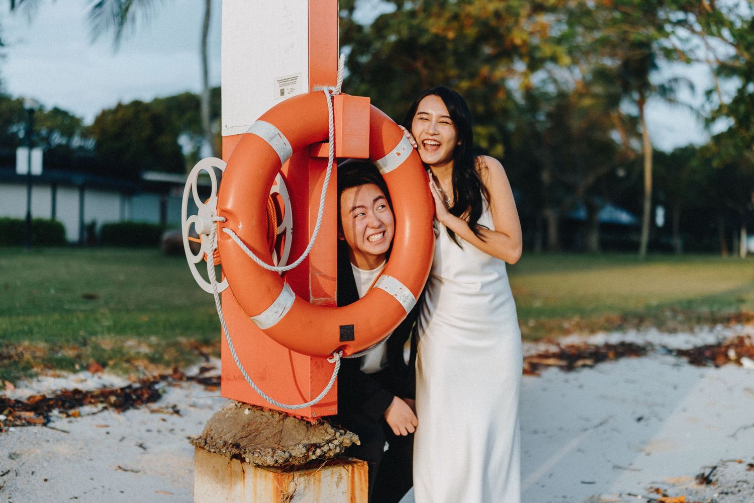 A couple shares a lighthearted moment with an orange life preserver at the beach.