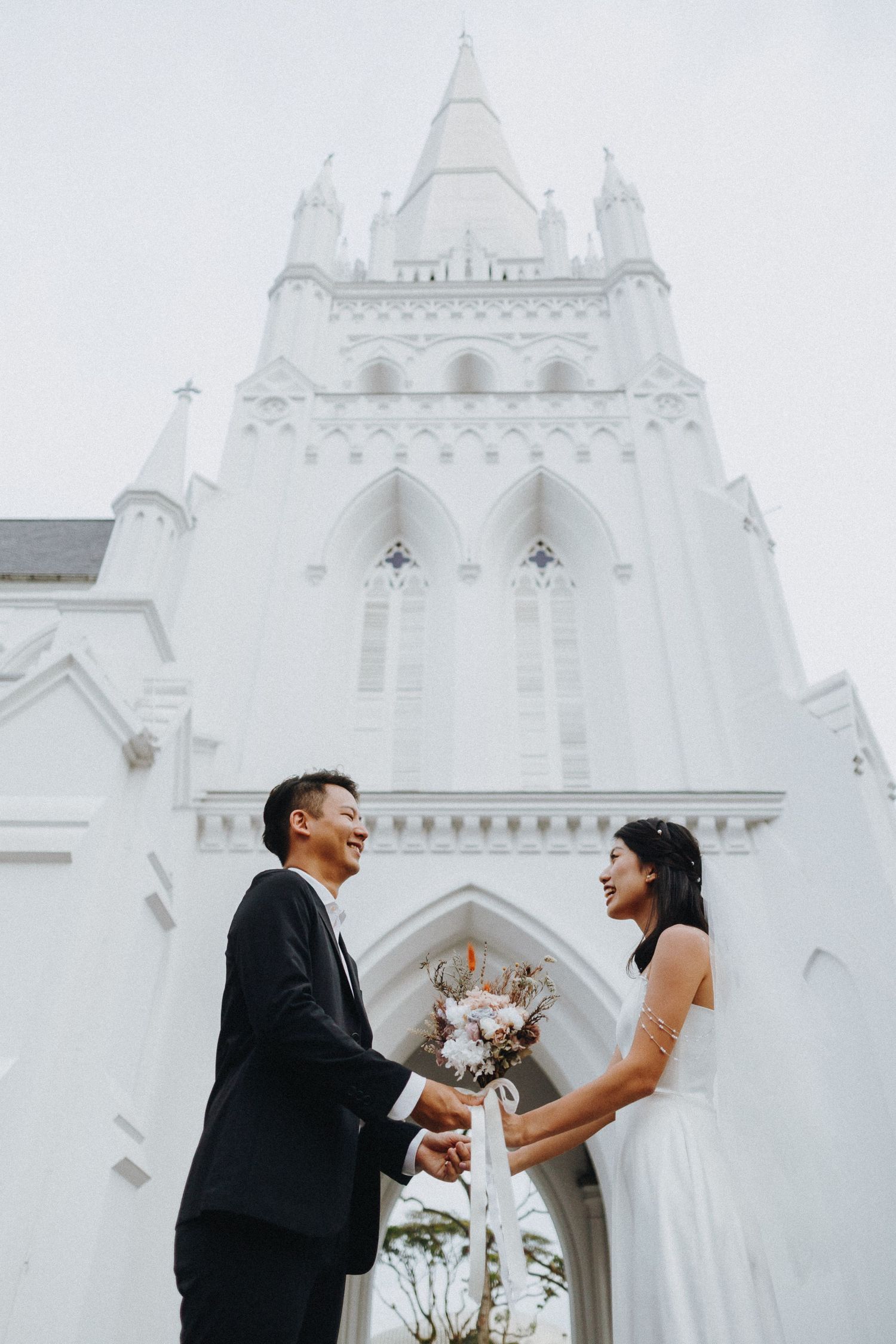 A couple shares a joyful moment in front of a stunning white gothic church spire.