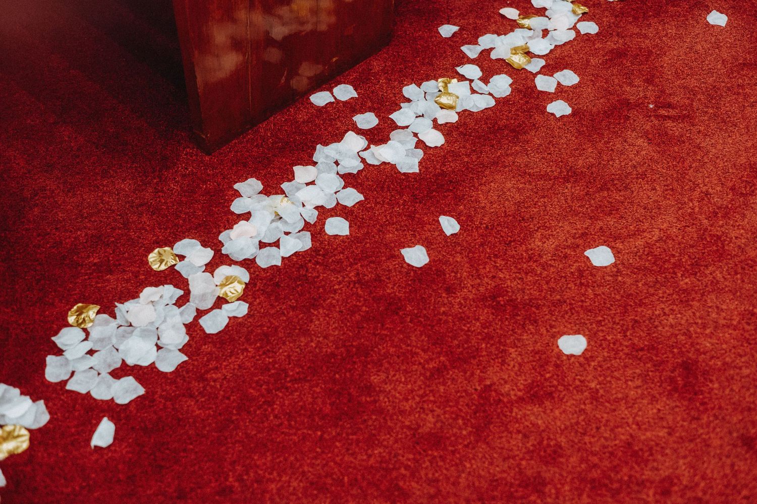 White and gold flower petals scattered along a red carpet aisle.
