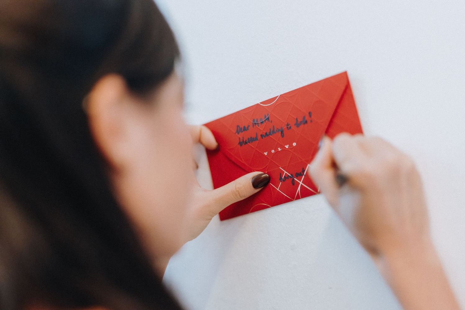 Woman holding a red envelope with handwritten text, examining the message closely with dark painted nails.