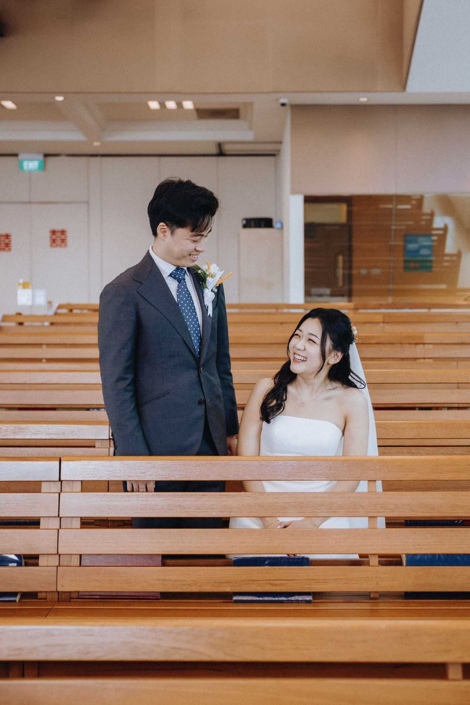 Bride and groom share a tender moment sitting in wooden church pews on their wedding day.