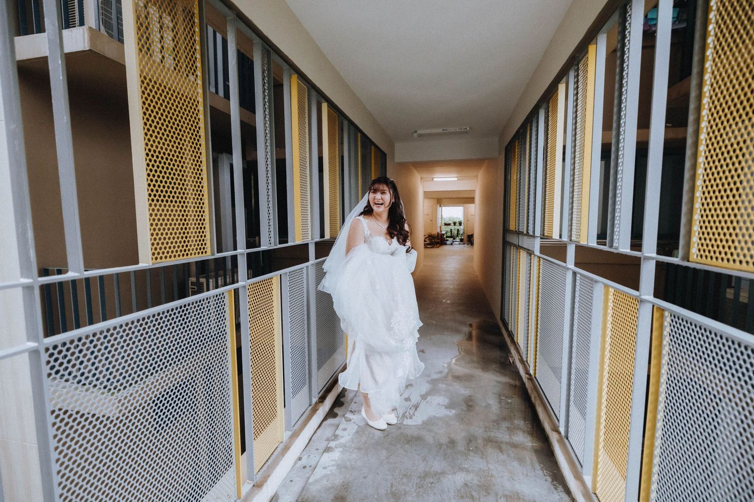 A bride in a flowing white gown walks down a modern hallway with gold and white striped walls.