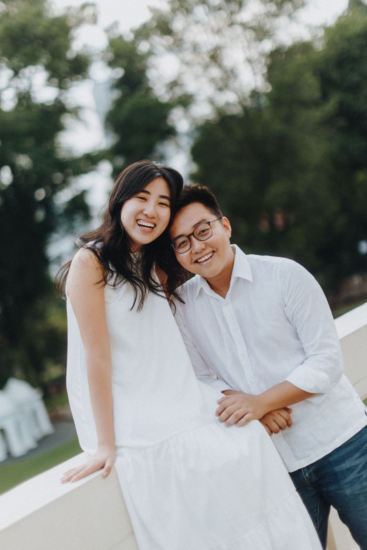 A couple in white clothing share a joyful moment together outdoors.