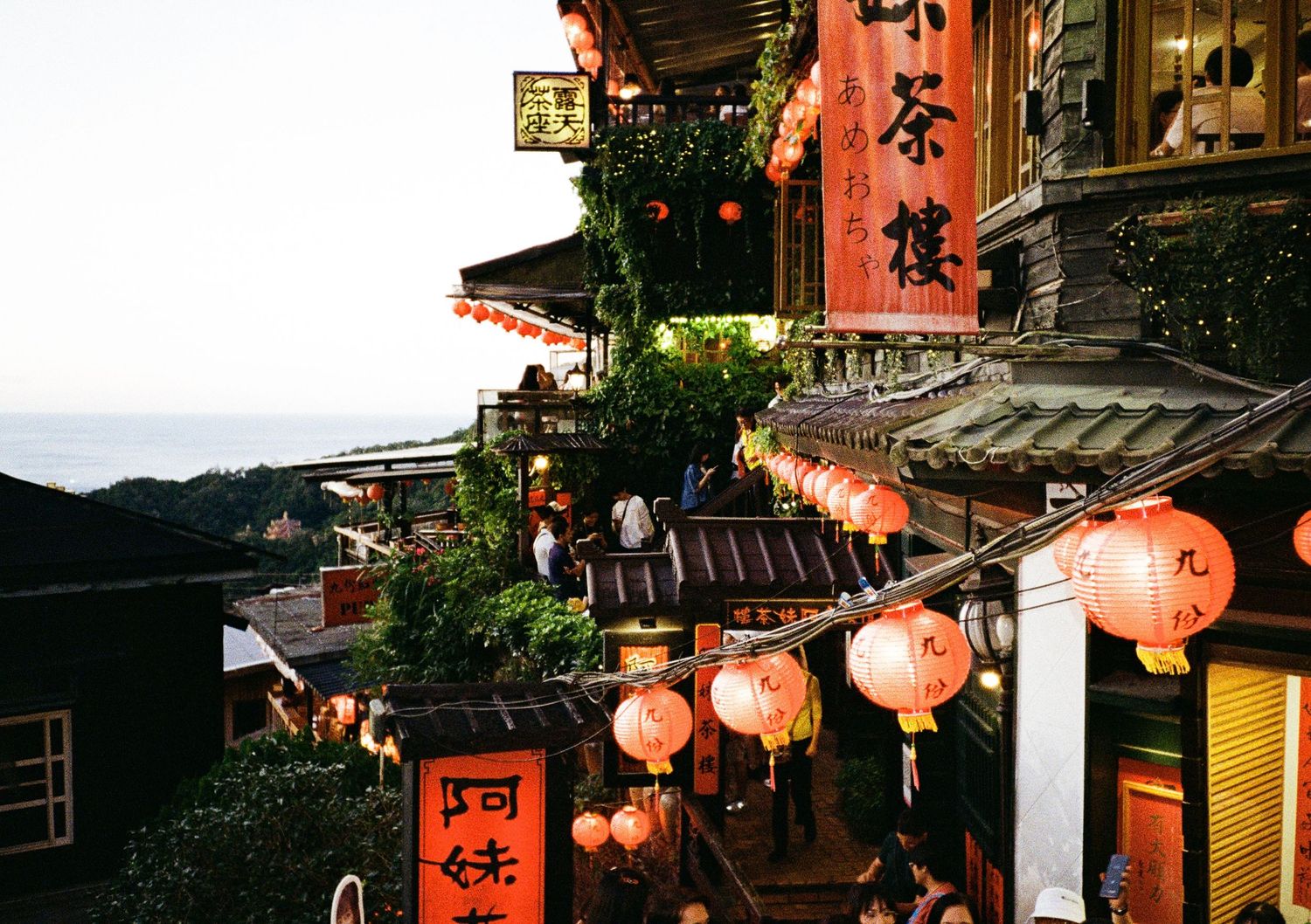 Traditional Japanese street with glowing red lanterns hanging along storefronts at dusk.