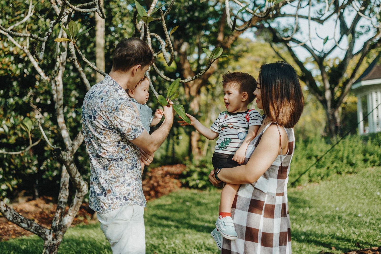 Family enjoying time together in a sunny backyard garden with trees and plants in the background.