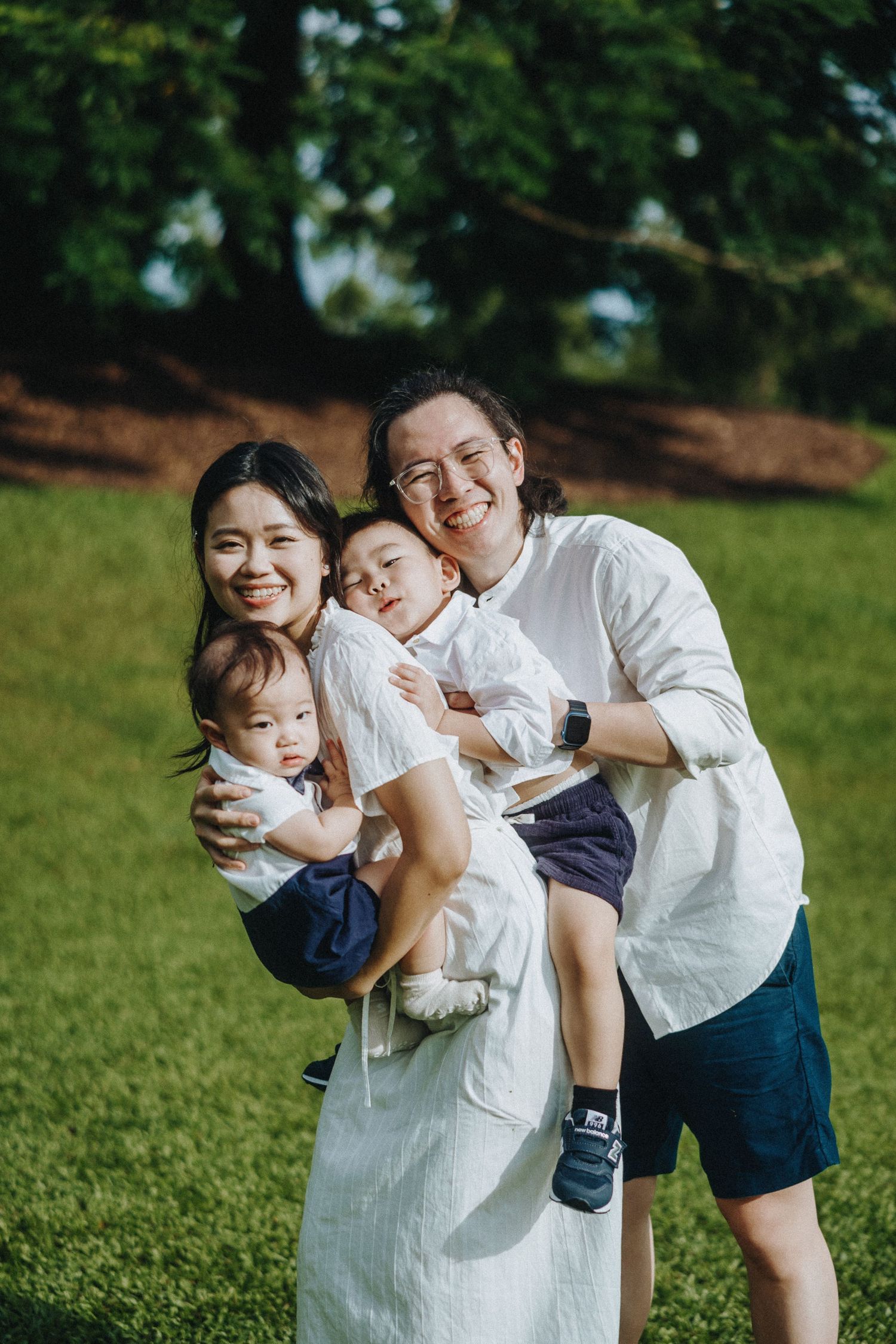 A family enjoys a playful moment together on a grassy lawn on a sunny day.