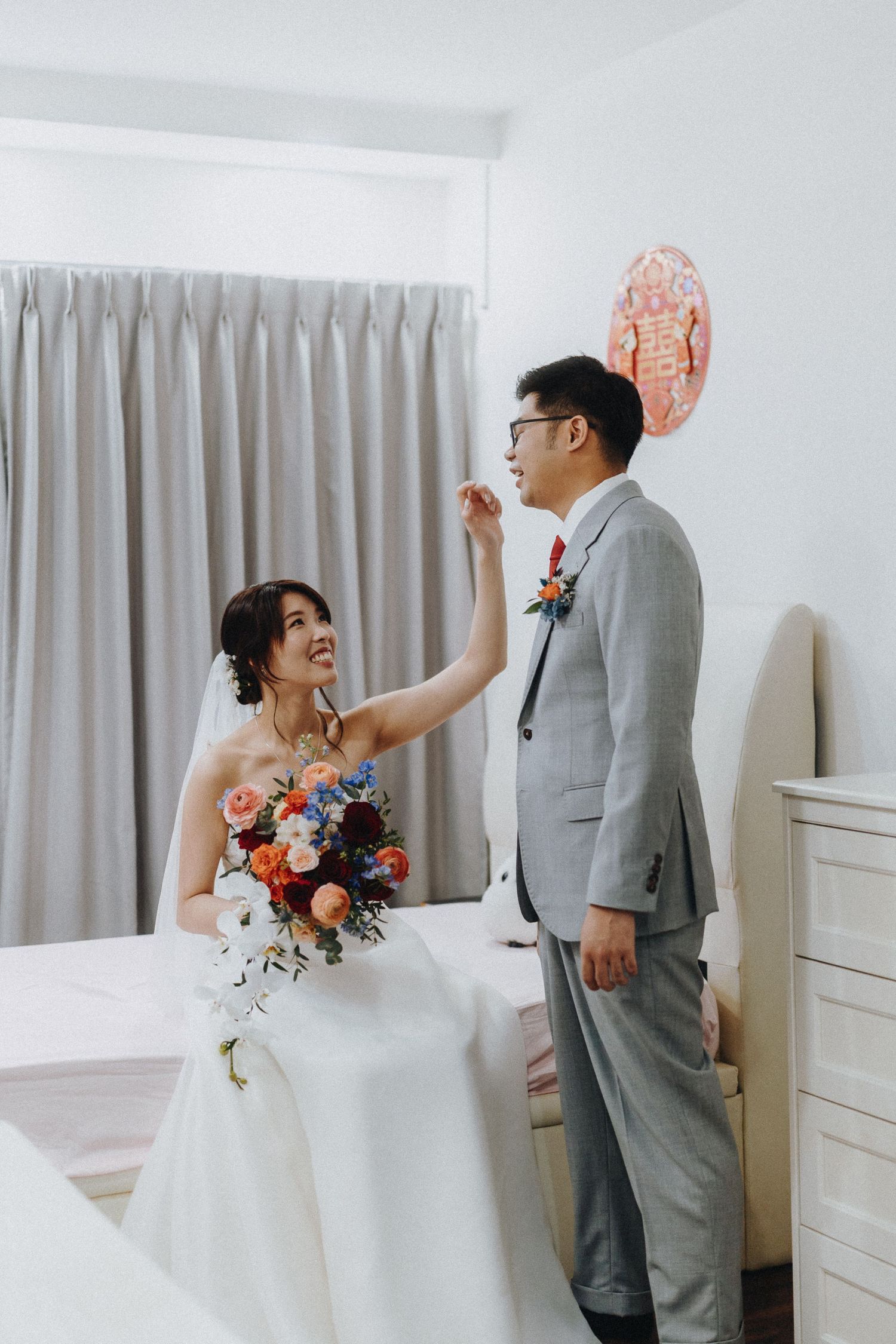 A couple sharing a joyful moment during their wedding day in a room with grey curtains and decorative balloons.