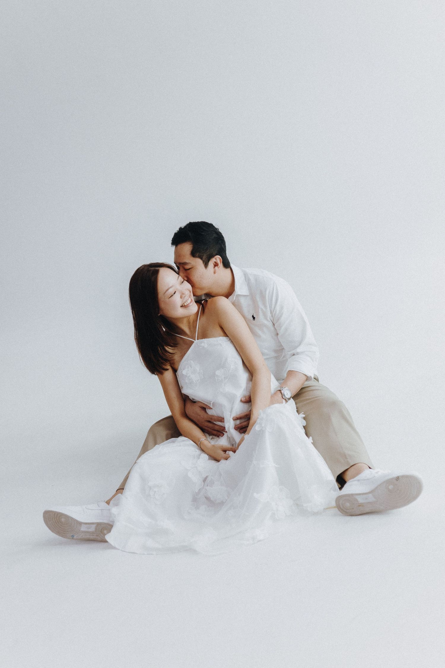 An intimate couple embraces while sitting on the floor in an artistic studio photoshoot.