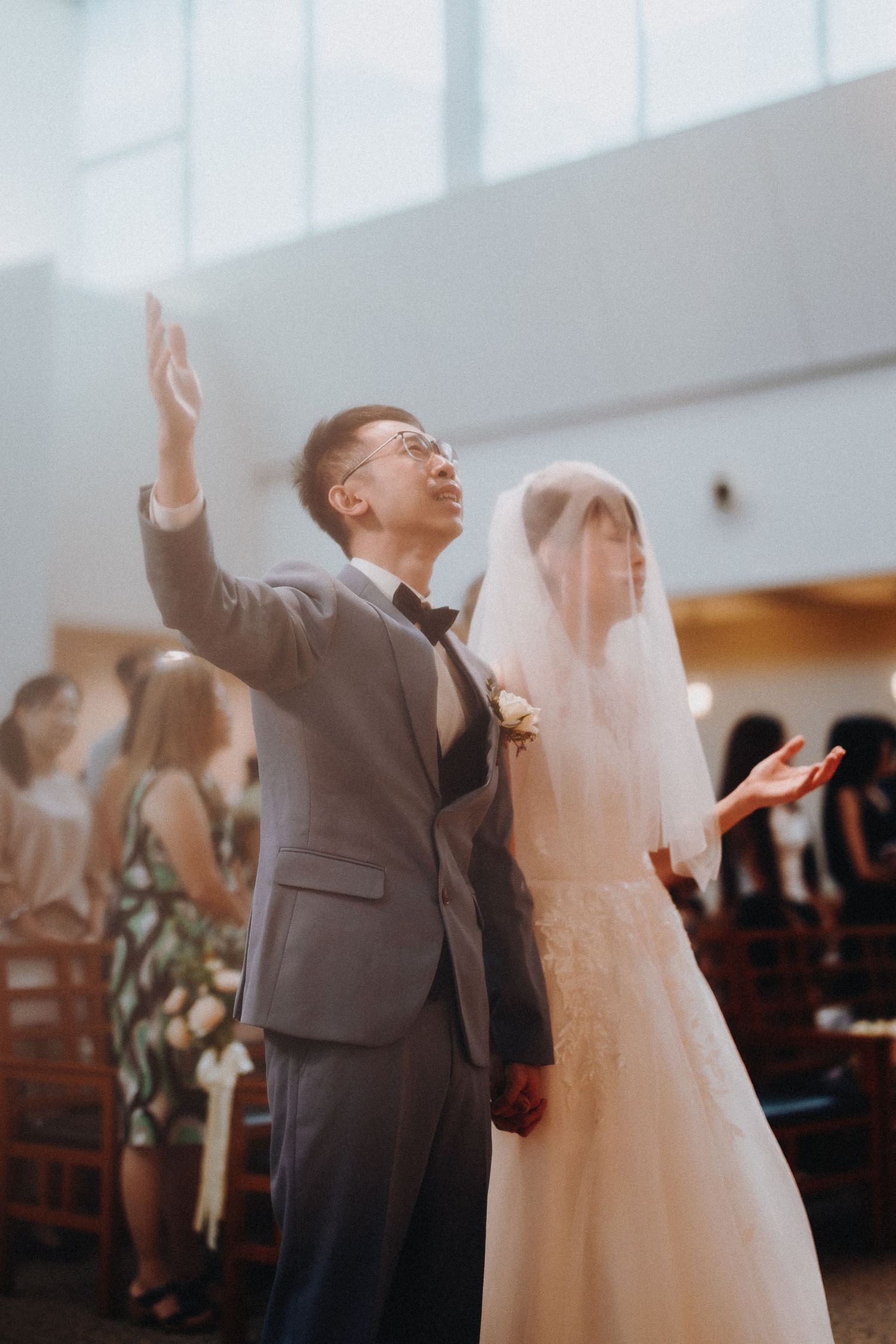 A couple stands together in worship during their wedding ceremony in a brightly lit church.