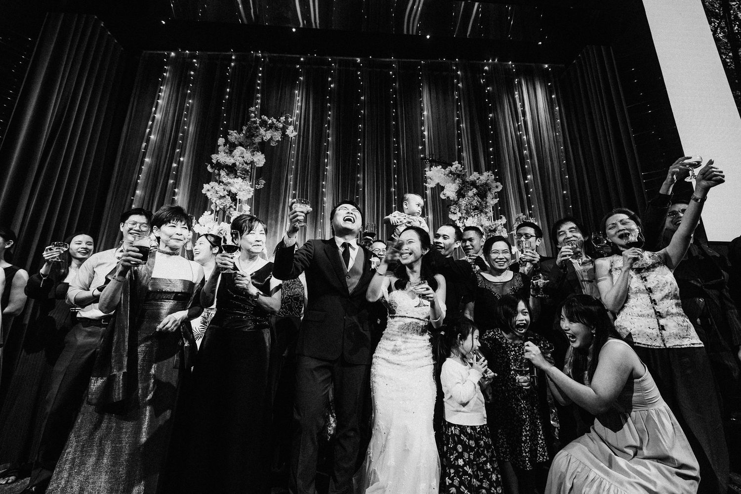 A black and white photo of wedding guests celebrating during the reception with dramatic lighting.